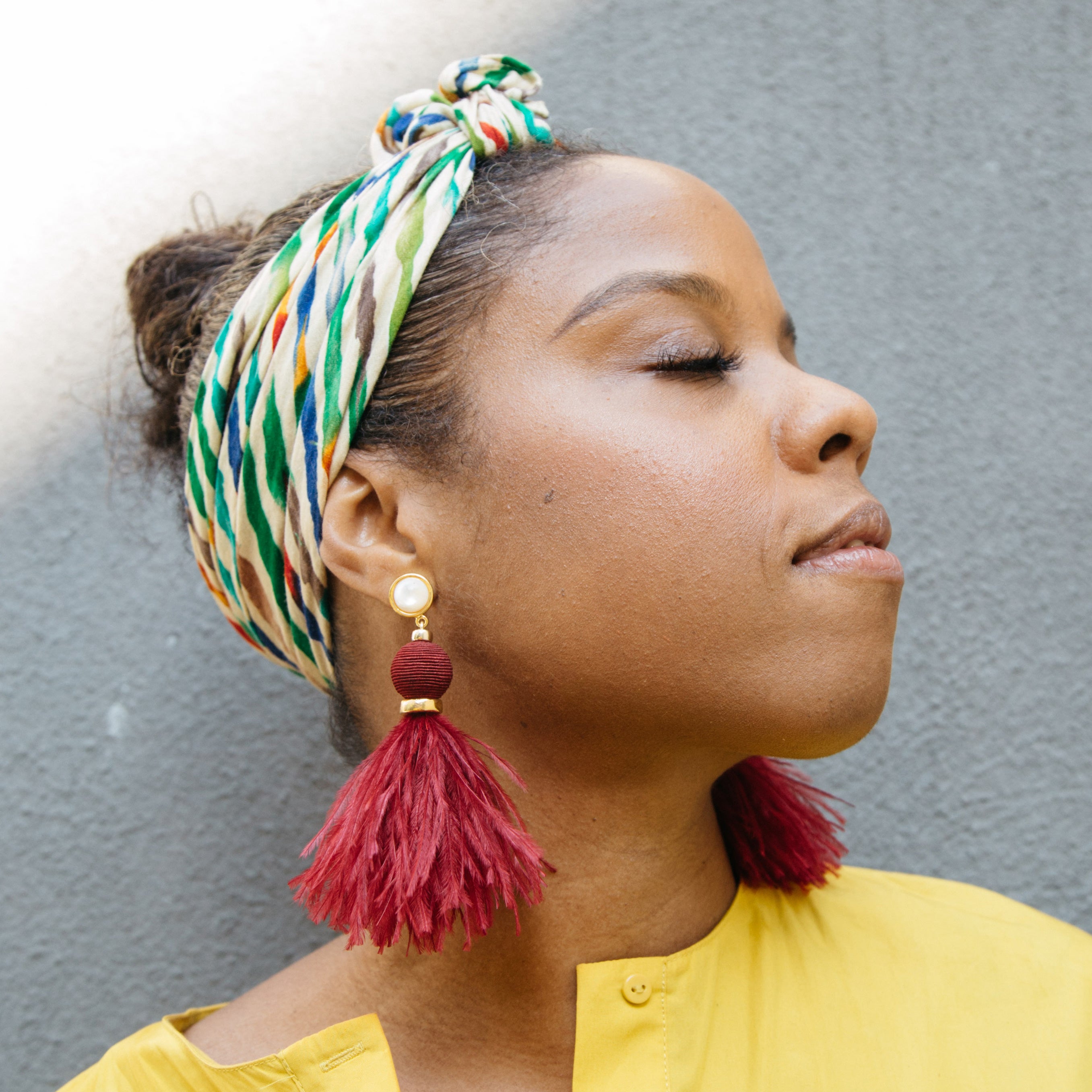 Woman wears yellow shirt colorful hair wrap and feather earrings