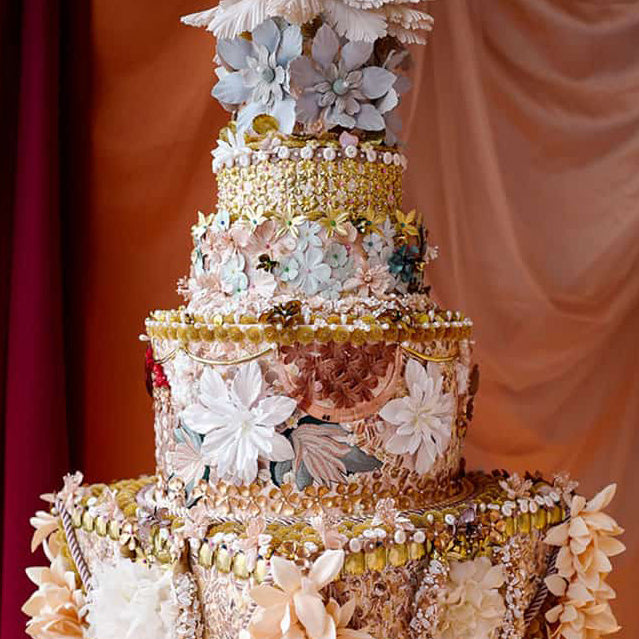Elaborate tiered cake with silk flowers on orange backdrop