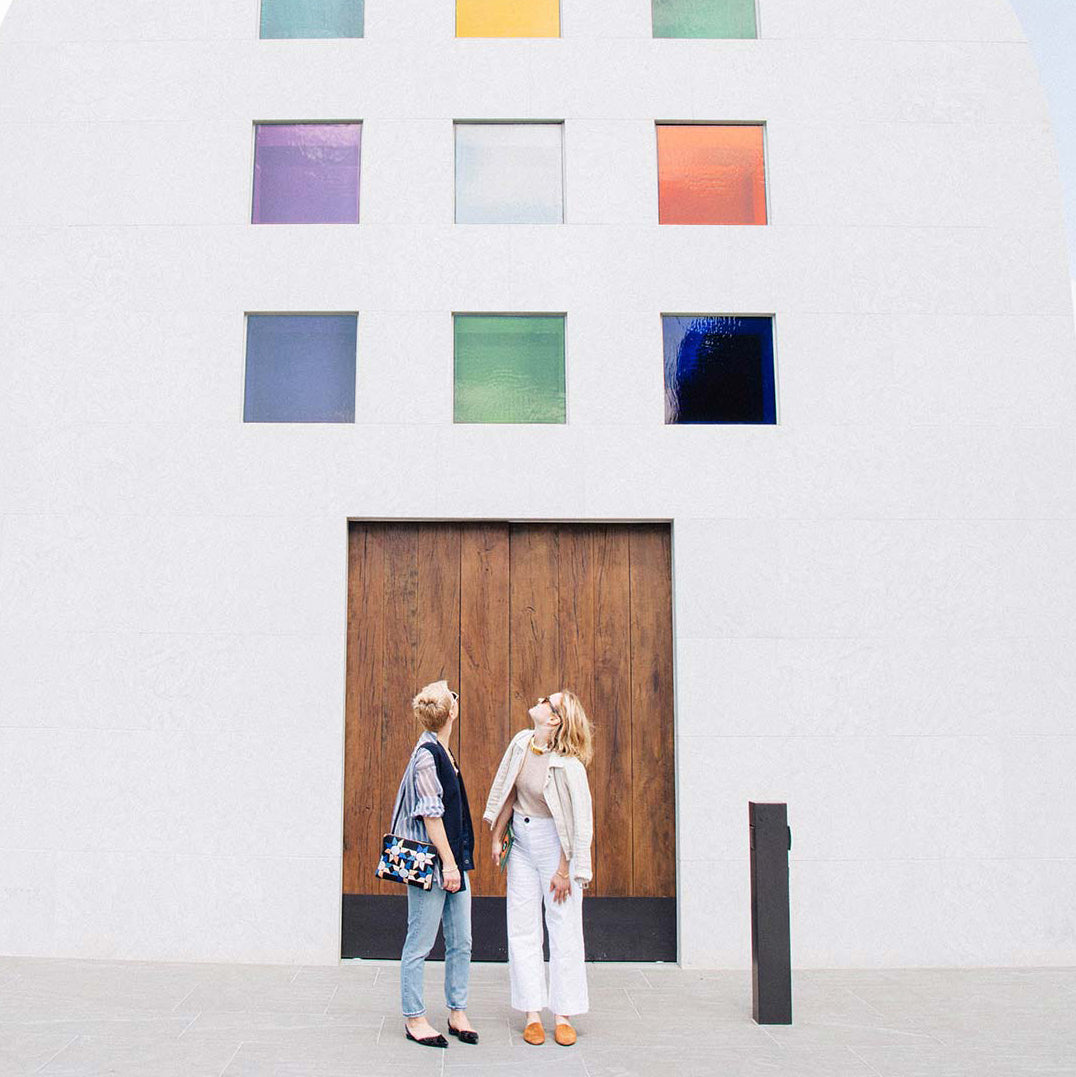 Fortunato twins stand in front of white building with wood door and colorful windows
