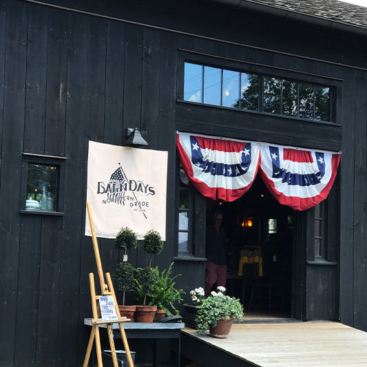 Black barn building with flags and plants out front