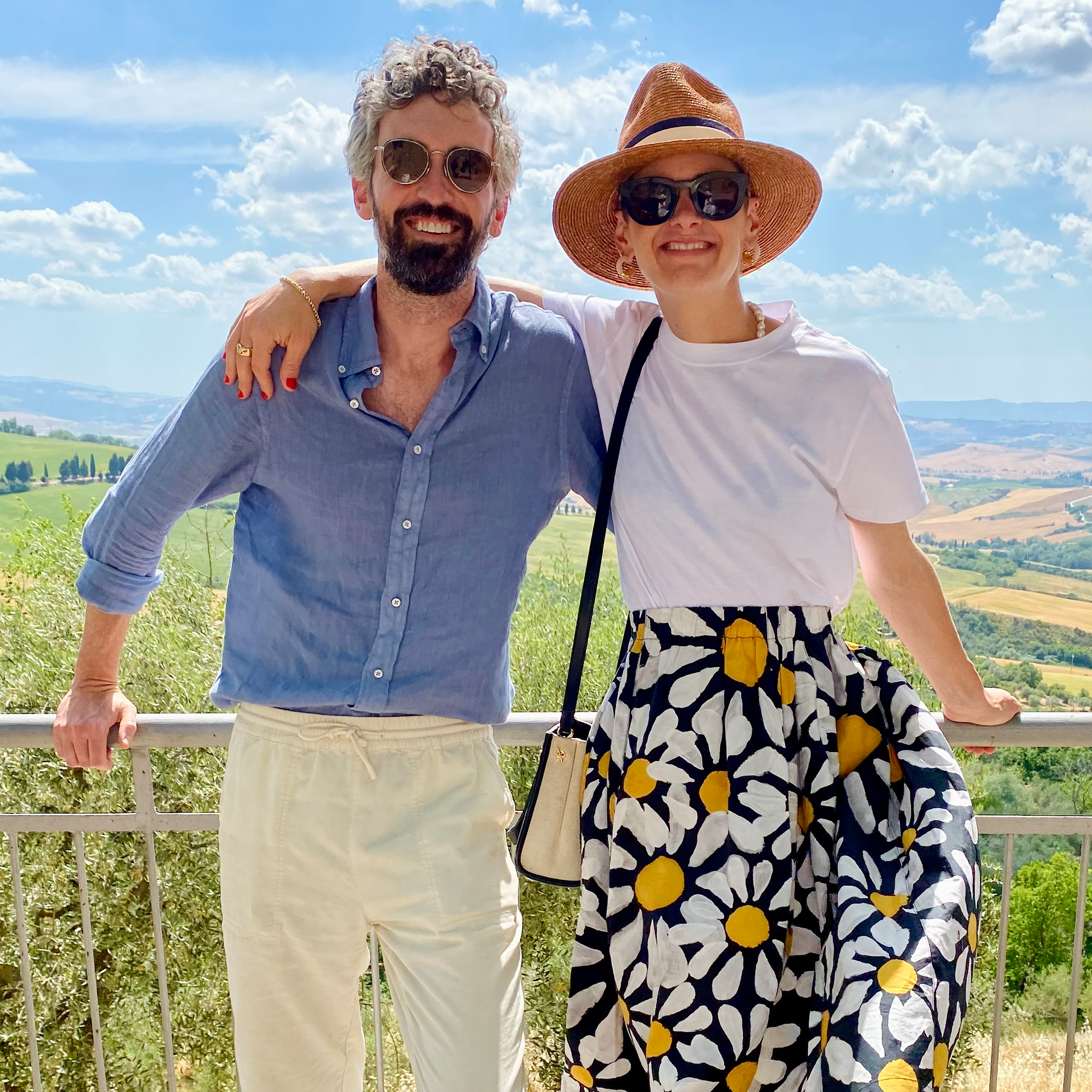 Lizzie and her husband Peter pose on a deck overlooking green fields and blue sky