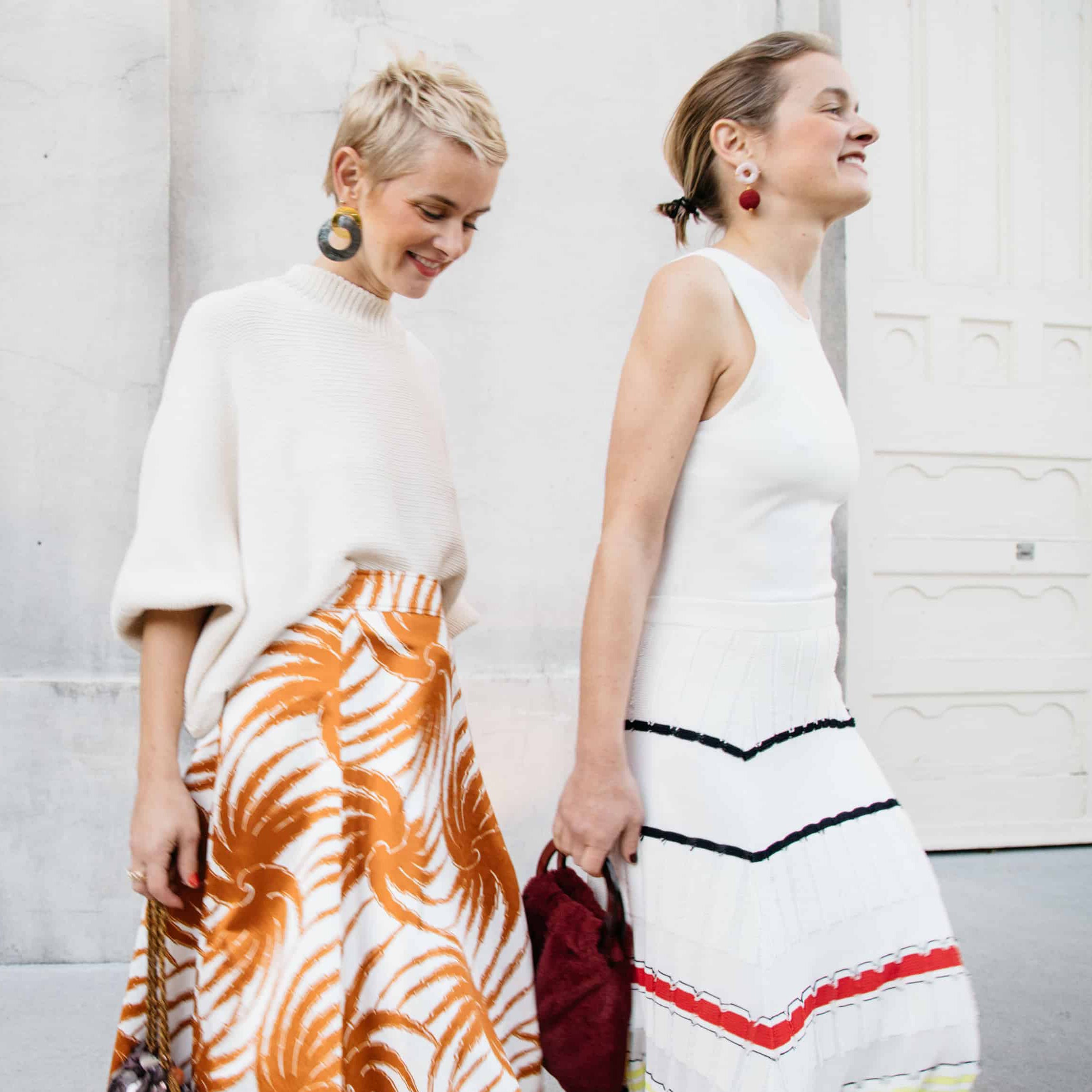 Twins Lizzie and Kathryn wear white sweater and printed skirt and knit dress, with statement earrings.