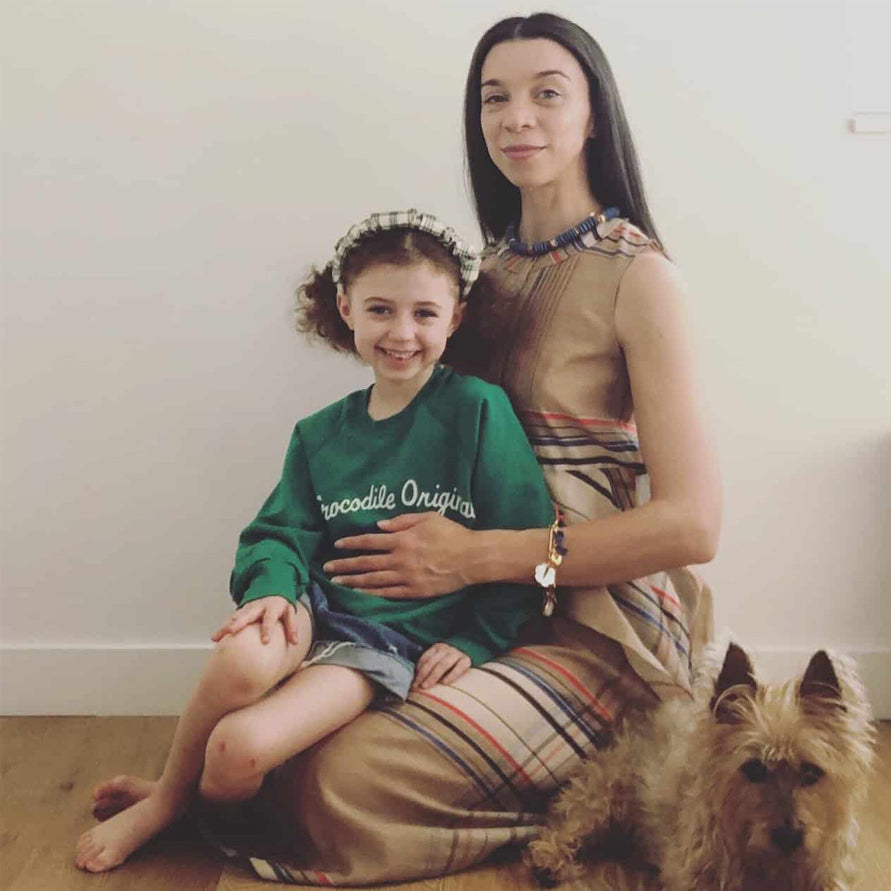 Mother and daughter sit on floor of house with small dog beside them