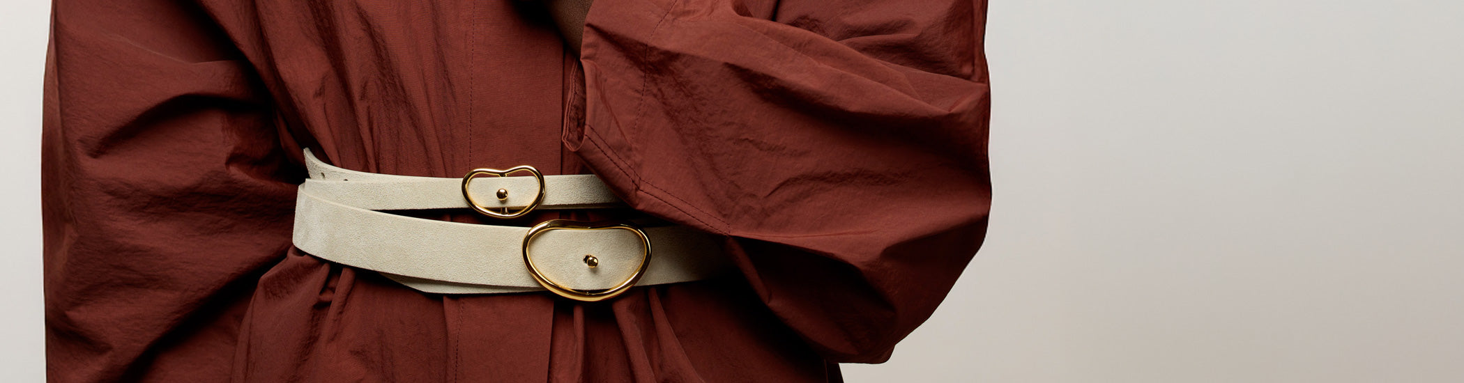 Close-up on model's waist wearing voluminous burgundy dress and two Georgia Belts in Light Stone Suede