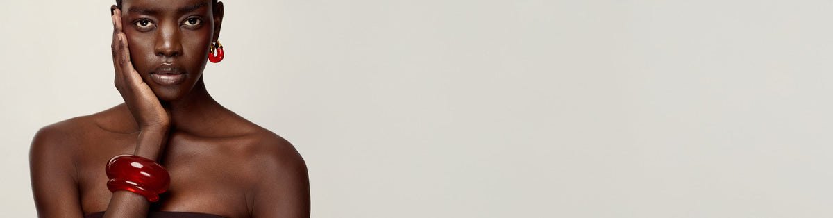 Model on grey backdrop wears Arc and Ridge Cuffs in Cherry with Organic Hoops in Cherry