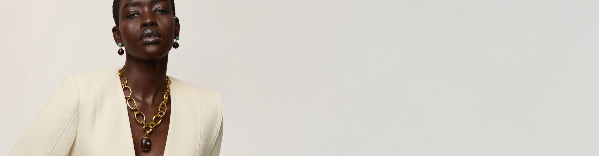 model on grey backdrop wears cream blazer with Beacon Charm Necklace and Umbria Earrings