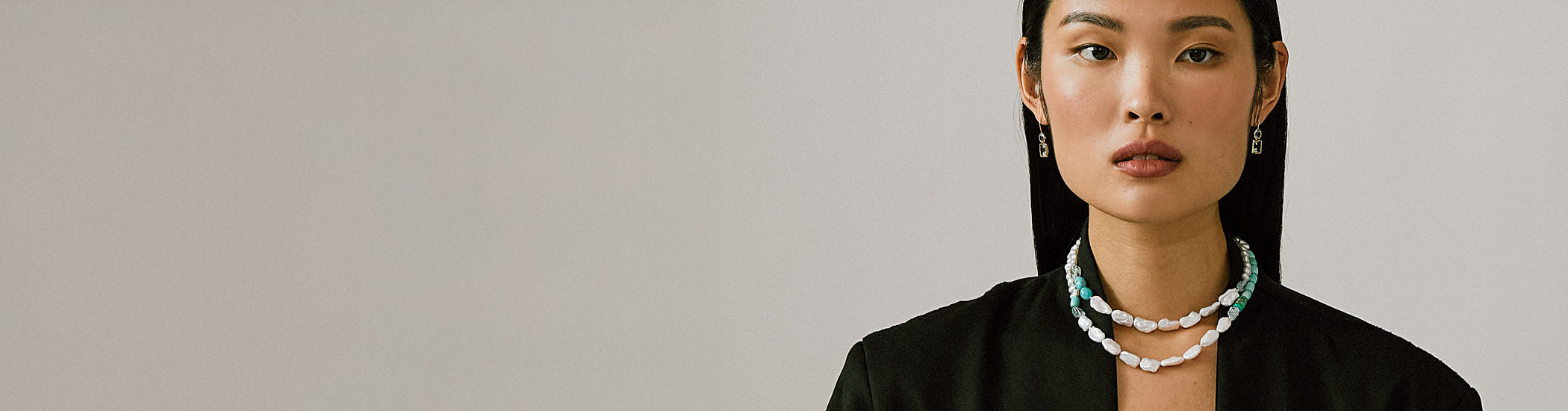 Model on grey backdrop wears 14k Gold Cabana Necklace in Turquoise & Pearl with black jacket