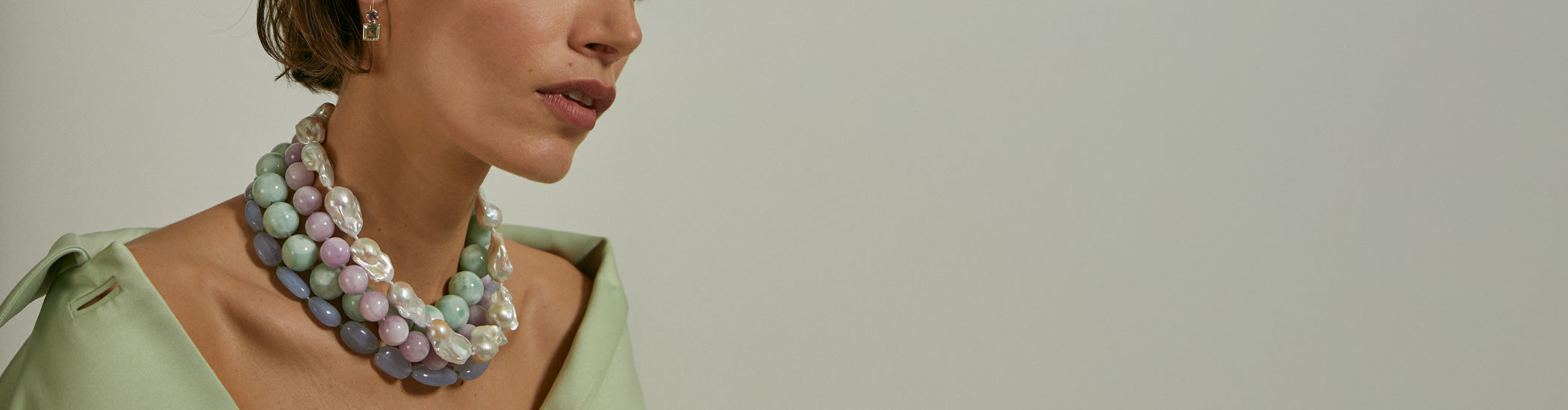 Model on grey backdrop wears chunky stack of fine bead necklaces in pastel colors