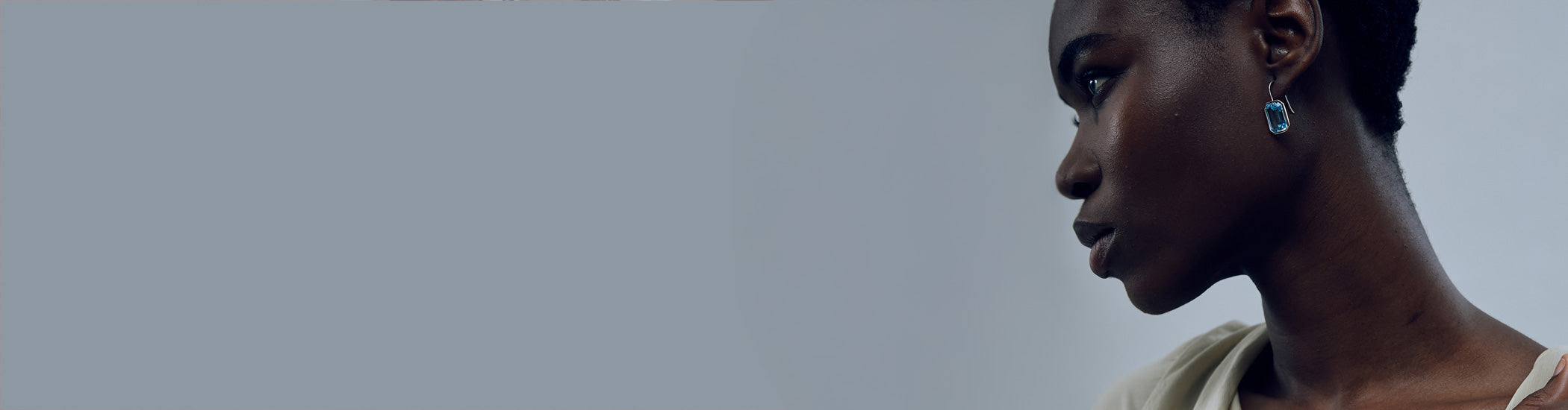 Model on grey backdrop wears Aria Earrings in Sky Blue Topaz