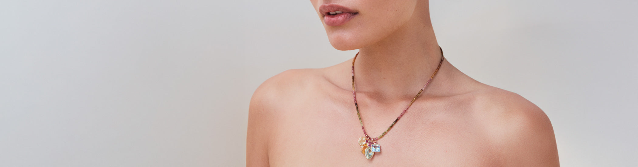 Model on grey backdrop wears Fine Mood Charm Necklace in Tourmaline Trove with bare skin