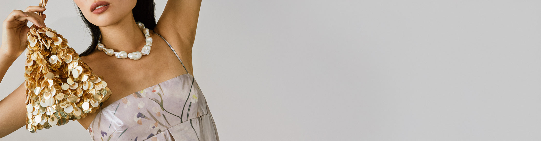 Model on grey backdrop with arms up holds gold Gala Bag and wears pearl necklace