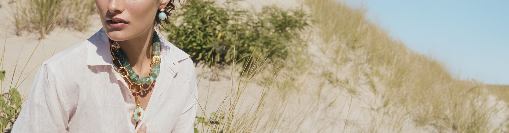 Model on dune grass wears pale pink shirt with Nautilus Collar and Porto Necklace in New Wave