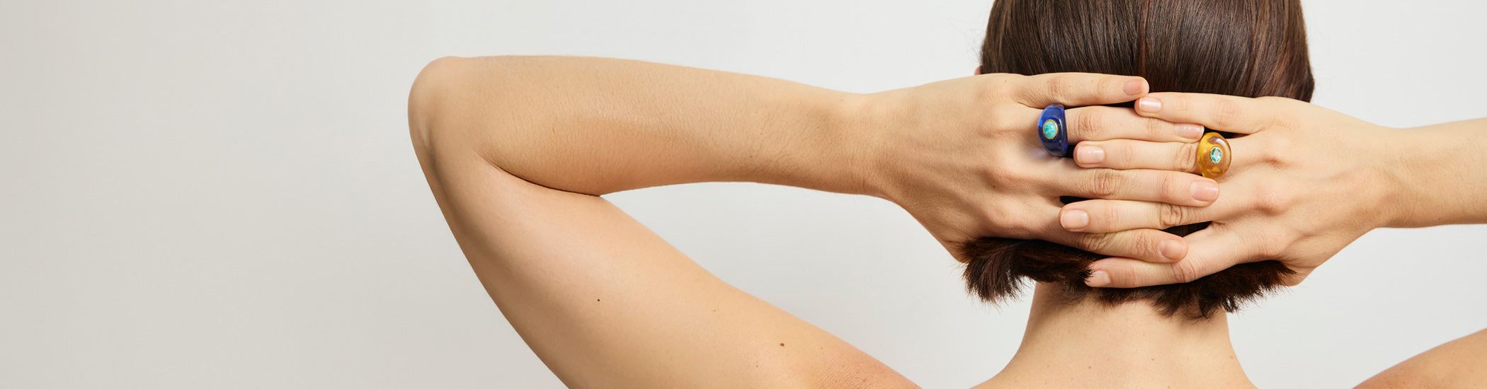Back of model with hands behind her head, wearing Monument Rings in Blue and Honey