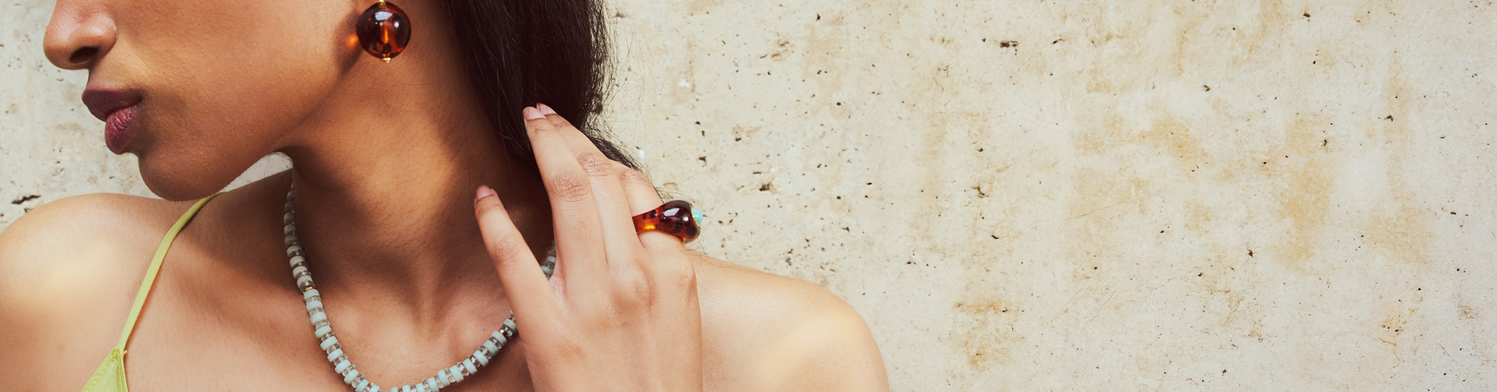 Model on tan stone backdrop holds hand to neck and wears Monument Ring in Leopard