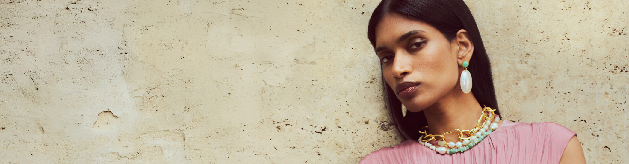 Model on tan stone backdrop wears Campana Earrings with Cabana Necklace and Porto Chain