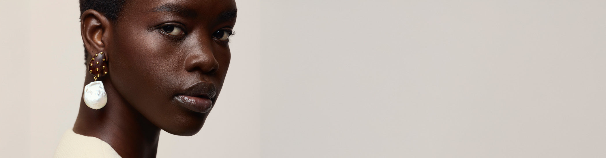Close-up on model's face on tan backdrop wearing Orbit Earrings in Pearl