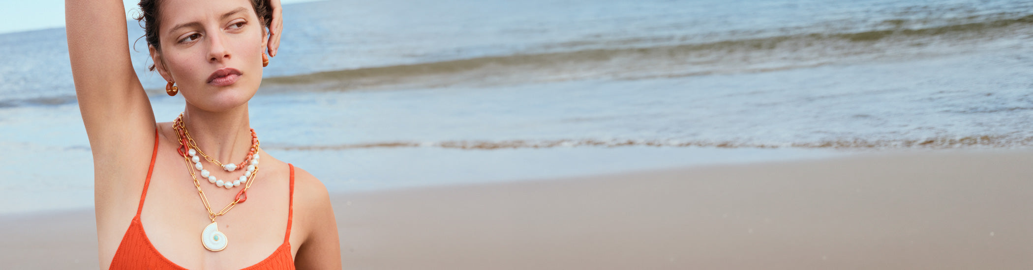 Model on beach wears red swimsuit with Sirena Shell Necklace and Zellige Hoops