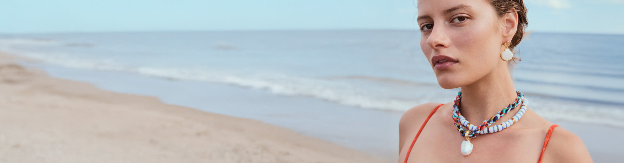 Model on beach wears Lido Necklace and Ibiza Collar with Luna Shell Earrings