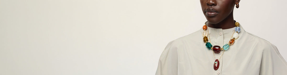 Model on grey backdrop wears red jacket with Granada and Hidden Stone Necklaces and Satsuma Earrings