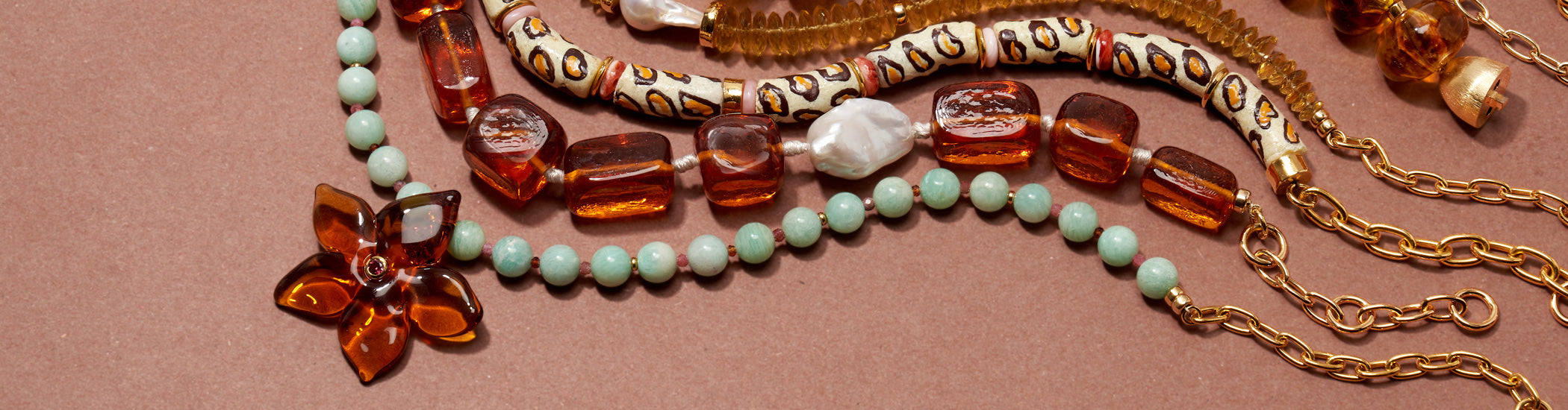 Model in profile on grey backdrop wears khaki shirt with assorted bead necklaces