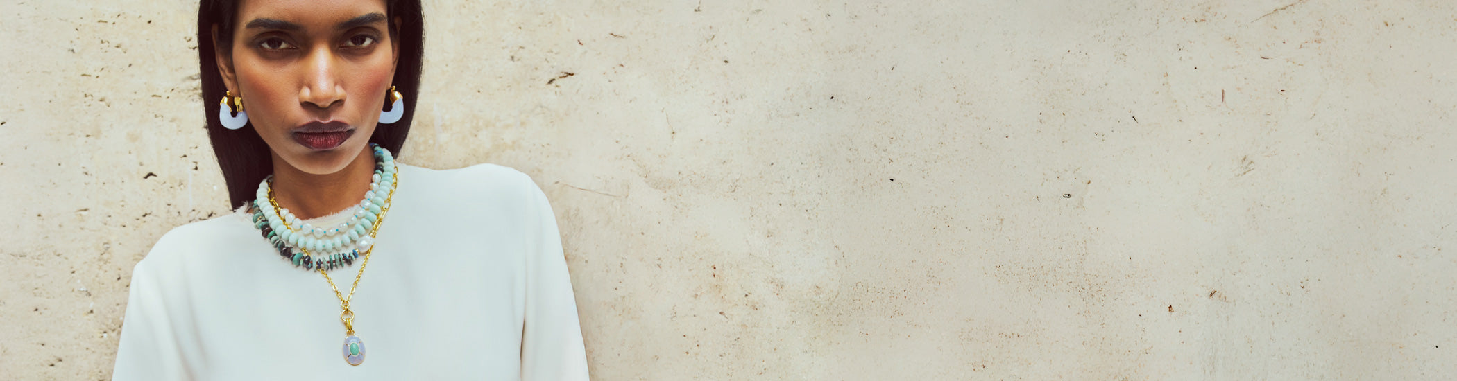 Model on stone backdrop wears white dress with Andamento Necklace and Zellige Hoops in Pearl