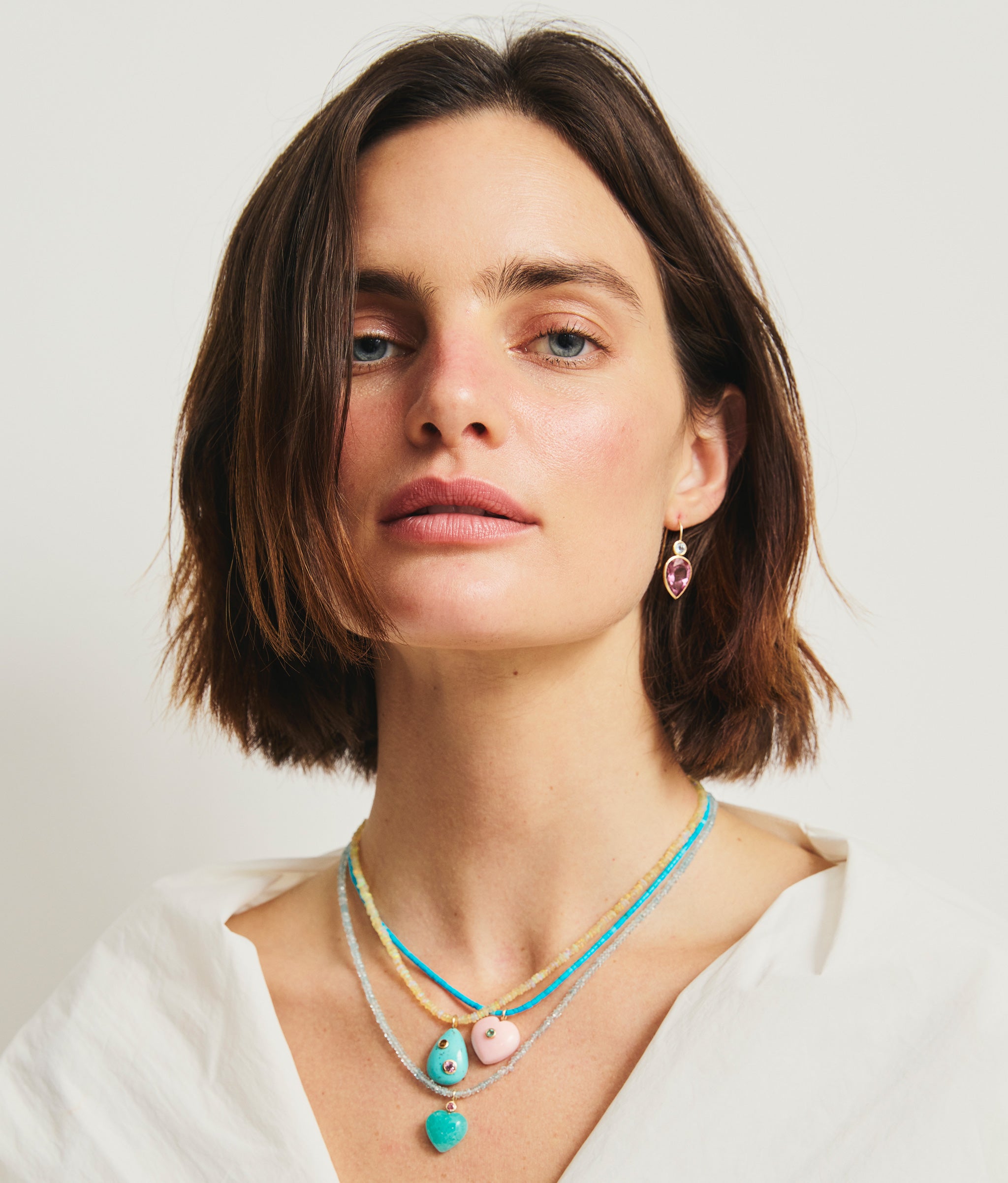 Model in white top wears Hera Earrings and three beaded necklaces with semiprecious charms