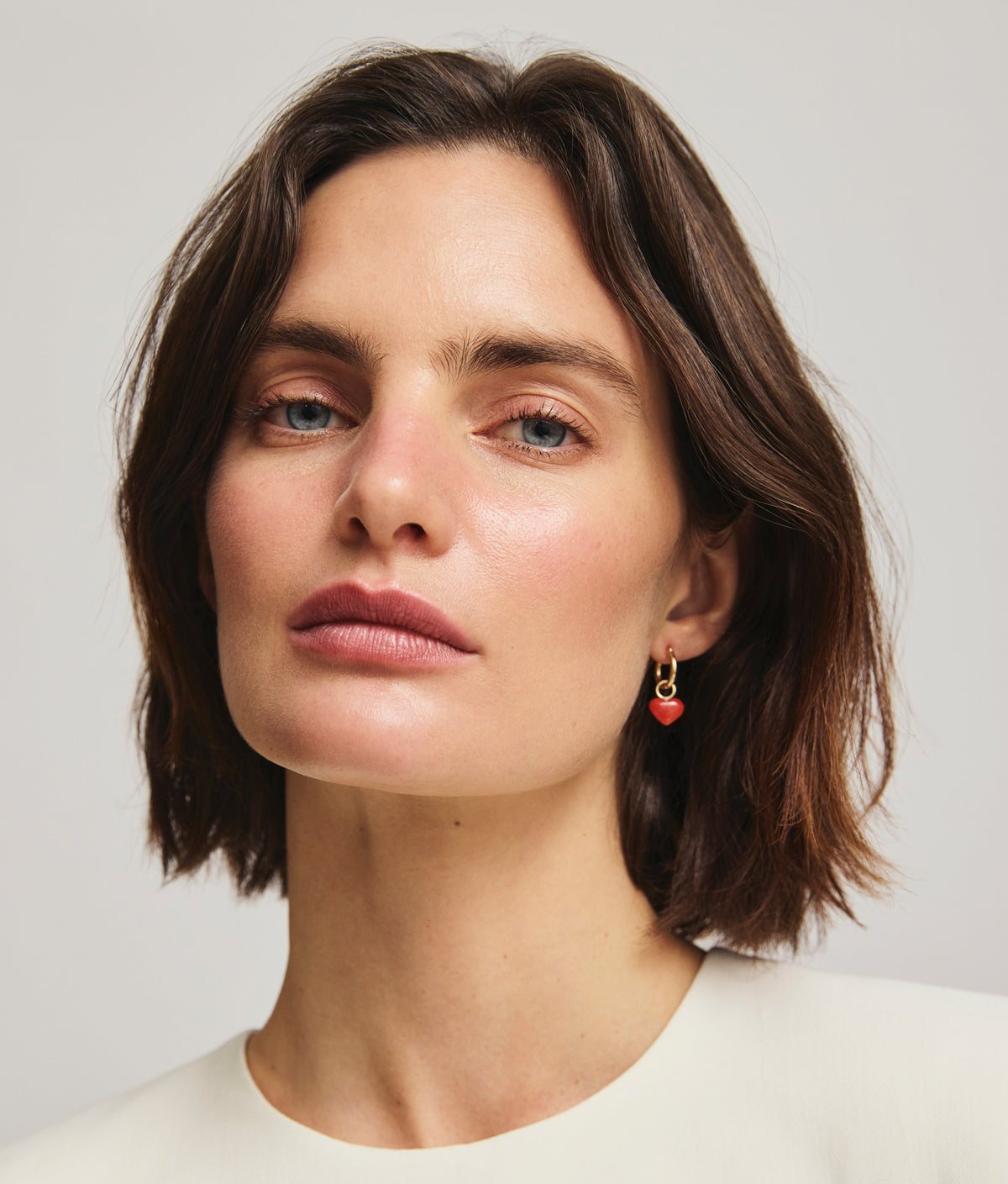 Model wears Gold Mood Hoops in Love Token, coral heart charm visible.
