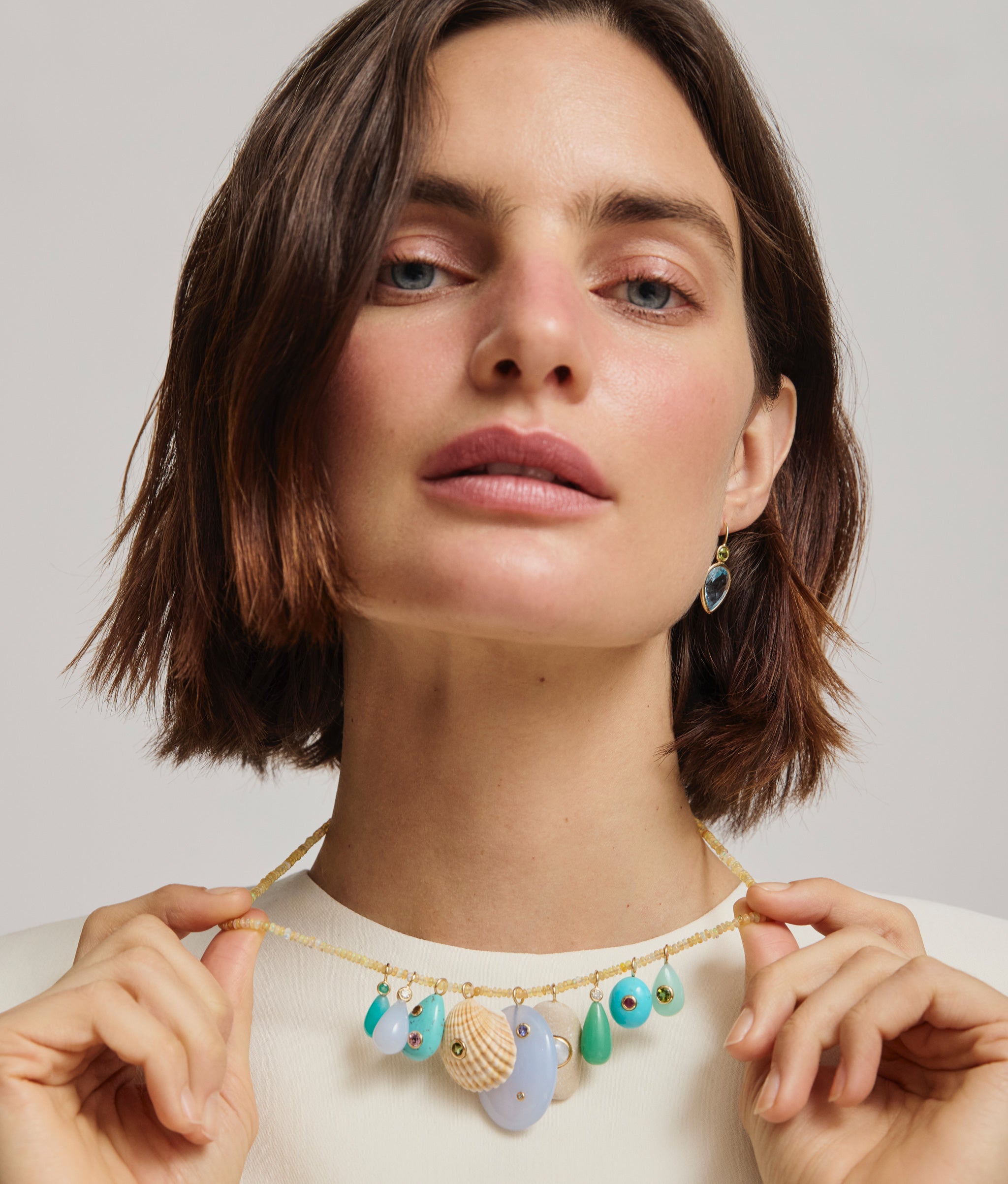 Model wears and holds opal bead necklace with assorted charms.