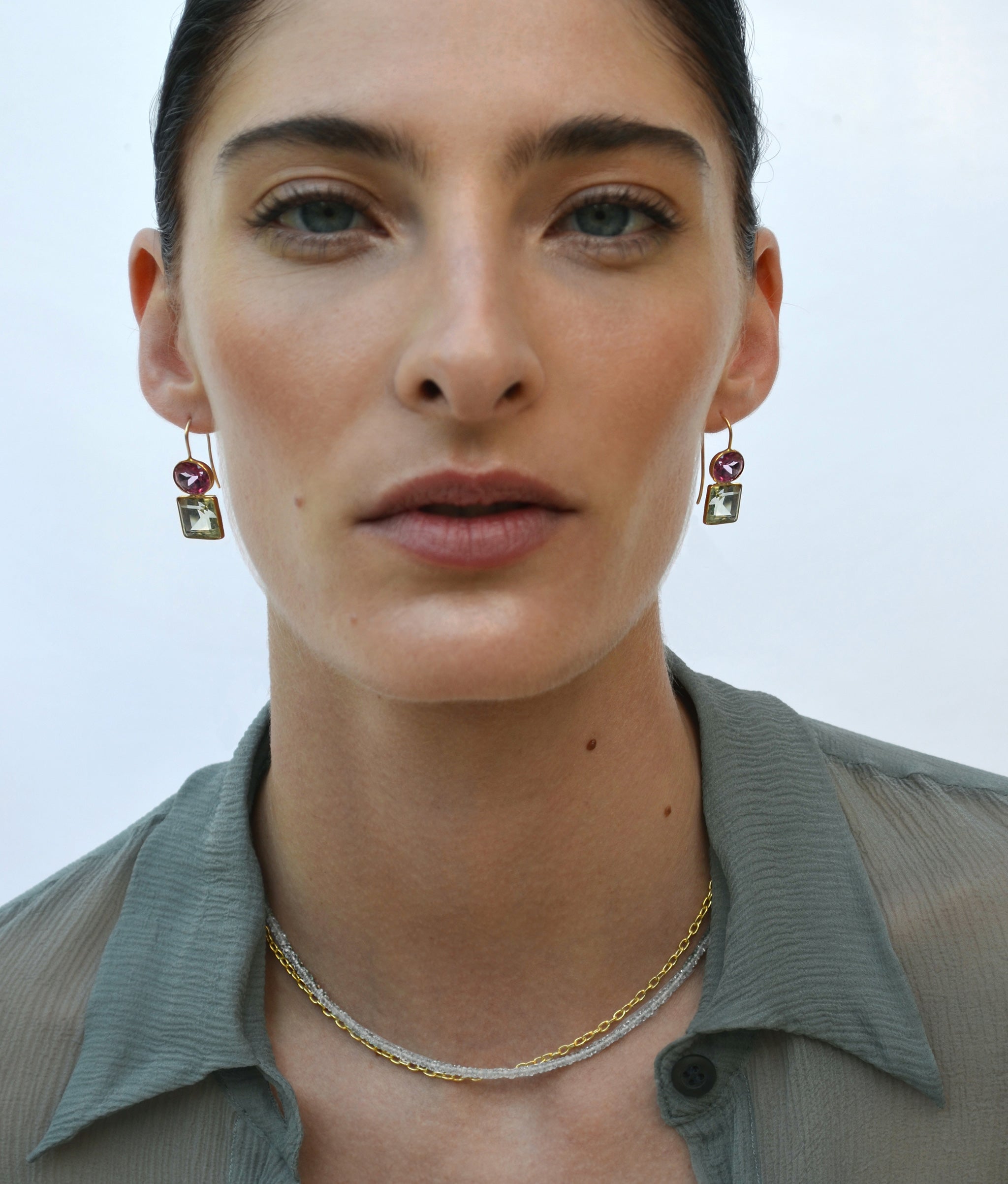 Model on blue backdrop wears gauzy top with Tiny Beaded Necklace in Light Aquamarine and gold chain