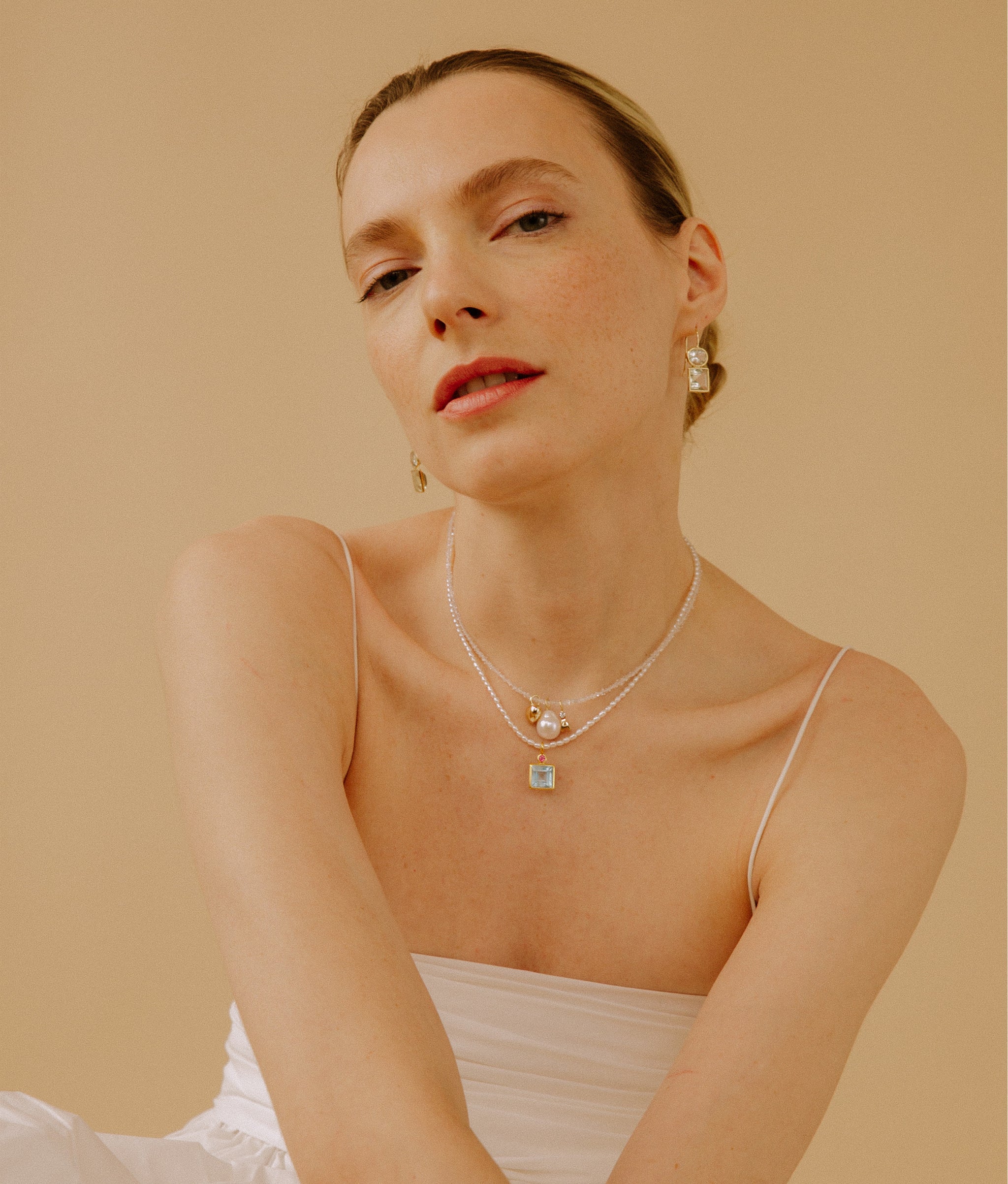 Model in white dress wears Tiny Beaded Pearl Necklace with semiprecious charms.