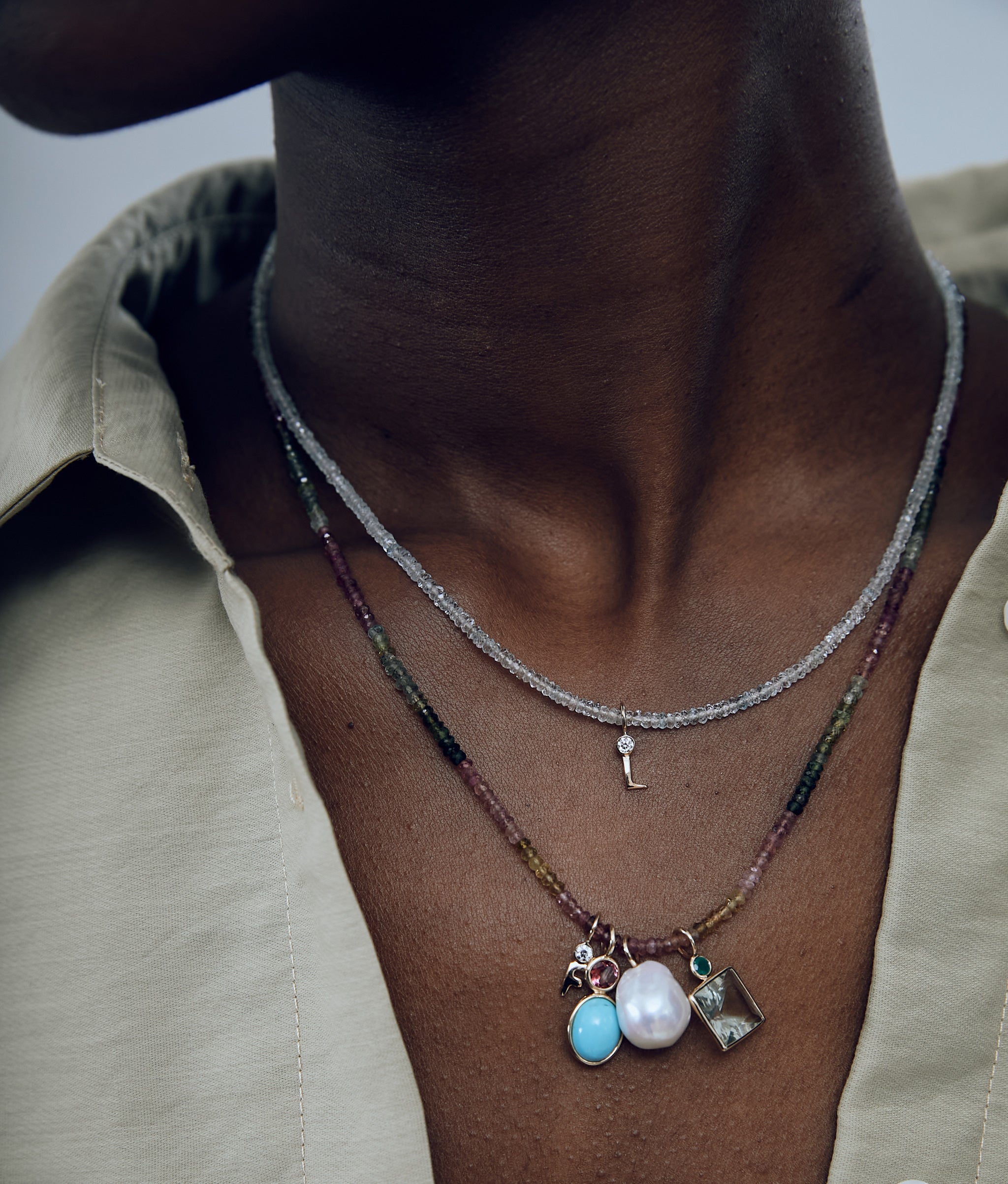 Close-up on model's neck wearing Tiny Beaded Aquamarine and Rainbow Tourmaline necklaces with charms.