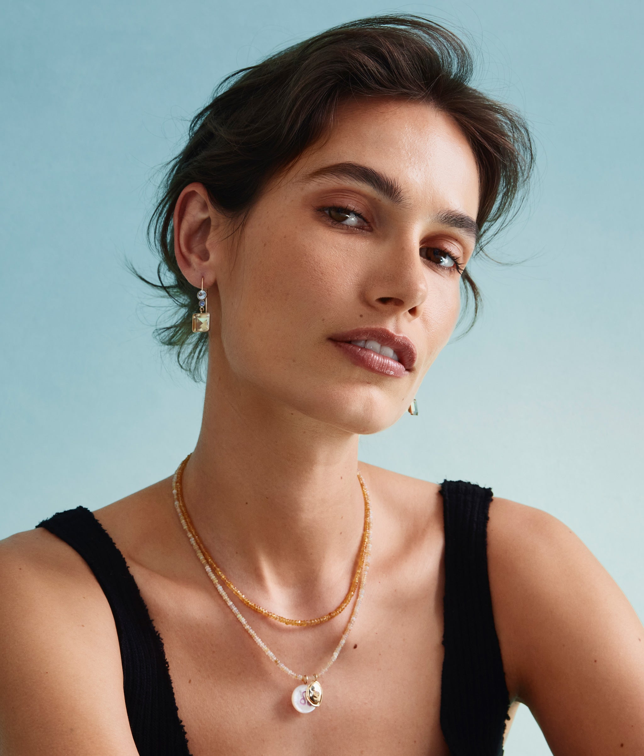 Model on blue backdrop wears black tank with Tiny Beaded 14k Gold Necklace in Yellow Sapphire
