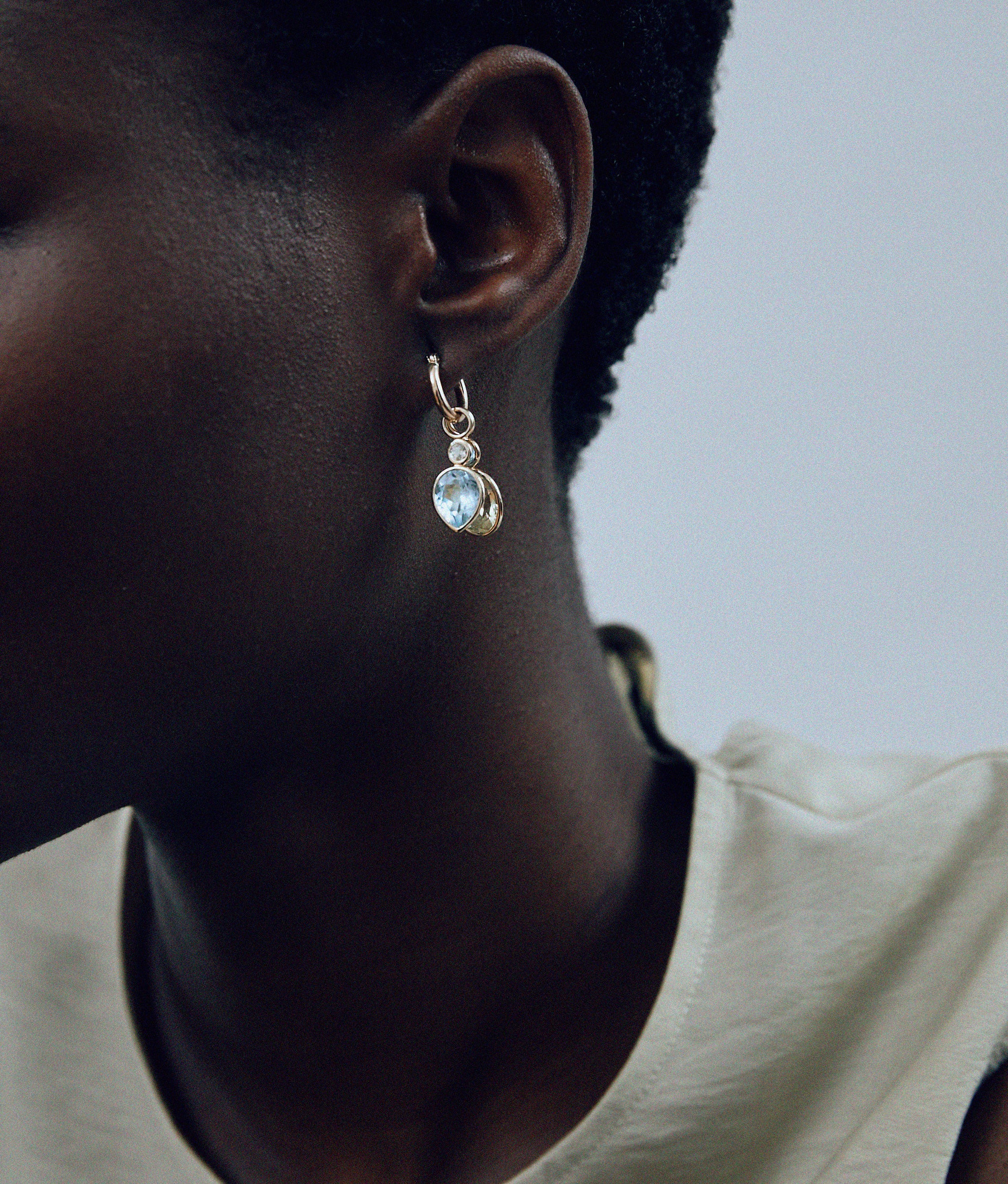 Model in close-up wears gold hoop with oval and teardrop semiprecious charms.