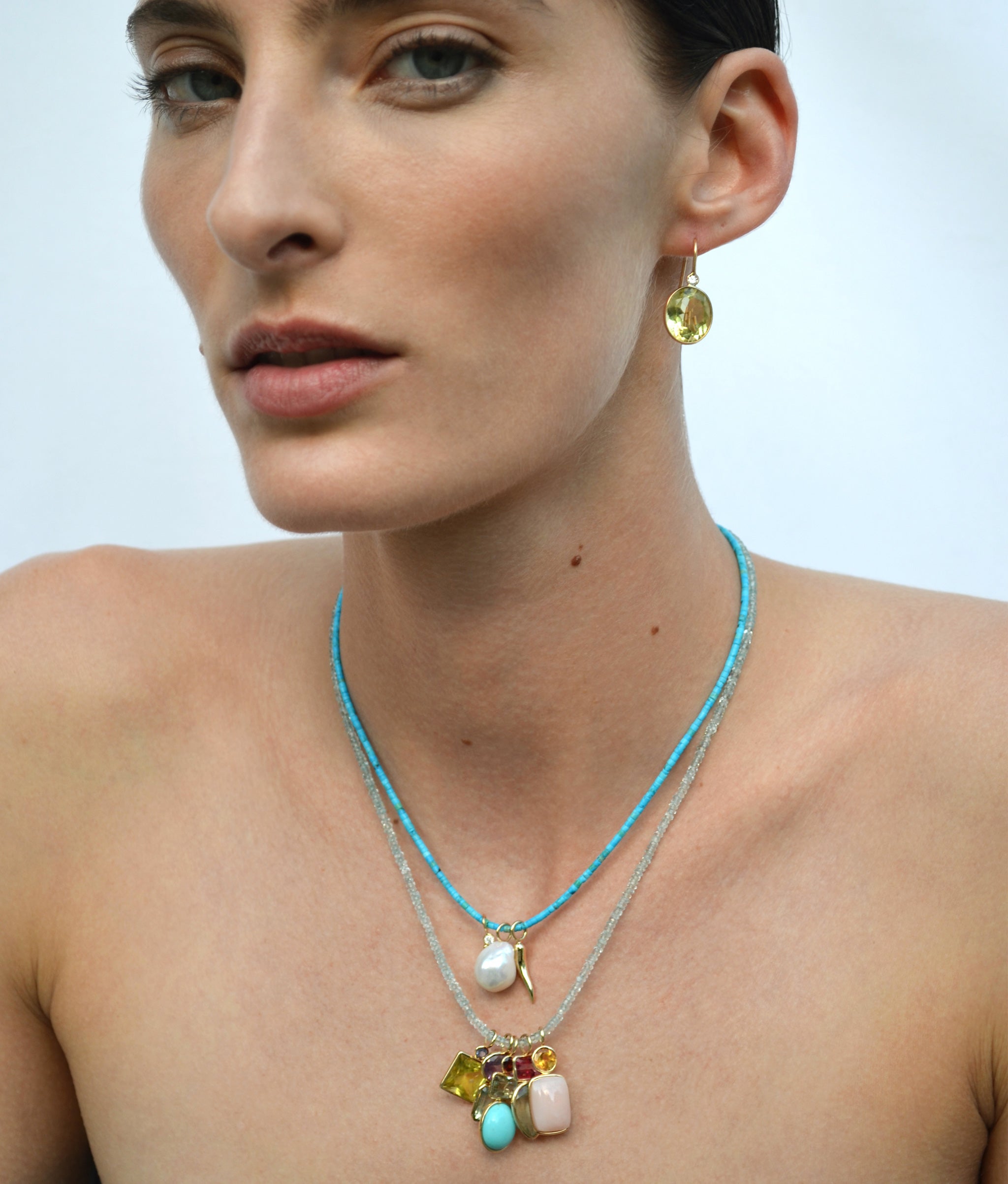 Model on sky blue backdrop wears two beaded necklaces with assorted semiprecious charms.