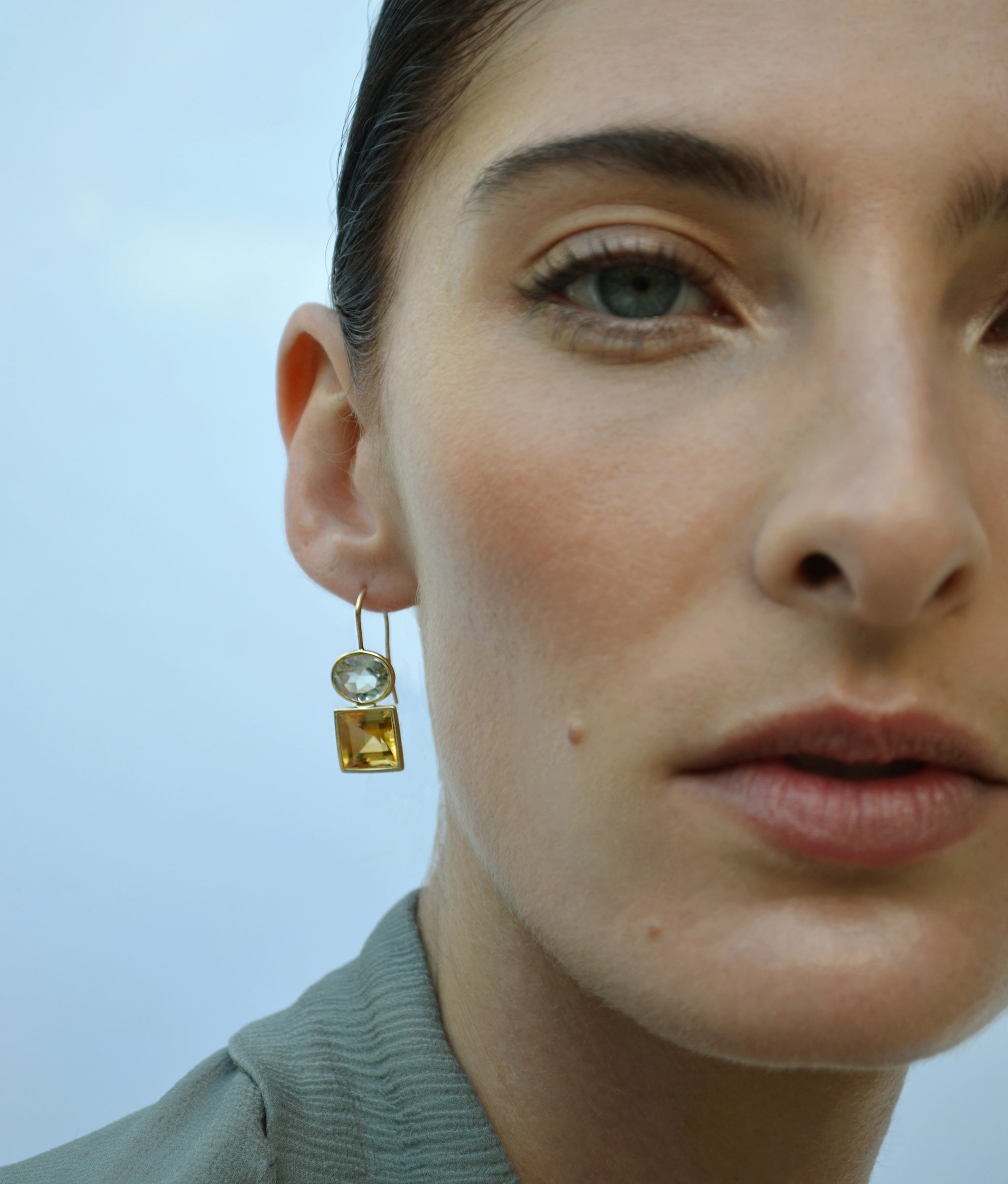 Model in close-up on blue background wears Duo Earrings in Green Amethyst and Citrine
