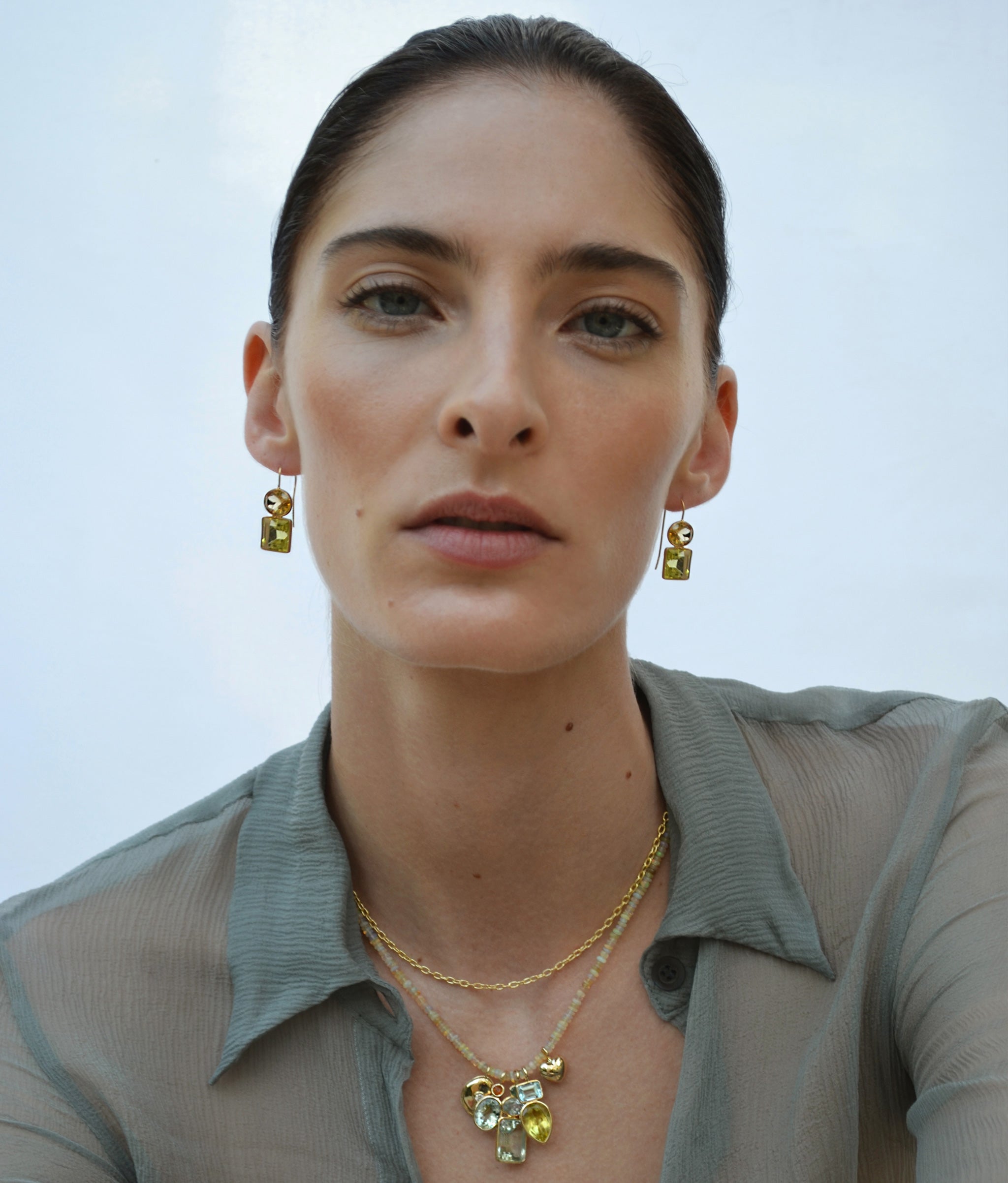 Model on blue backdrop wears gauzy top with Duo Earrings in Citrine and Lemon Quartz and beaded charm necklace
