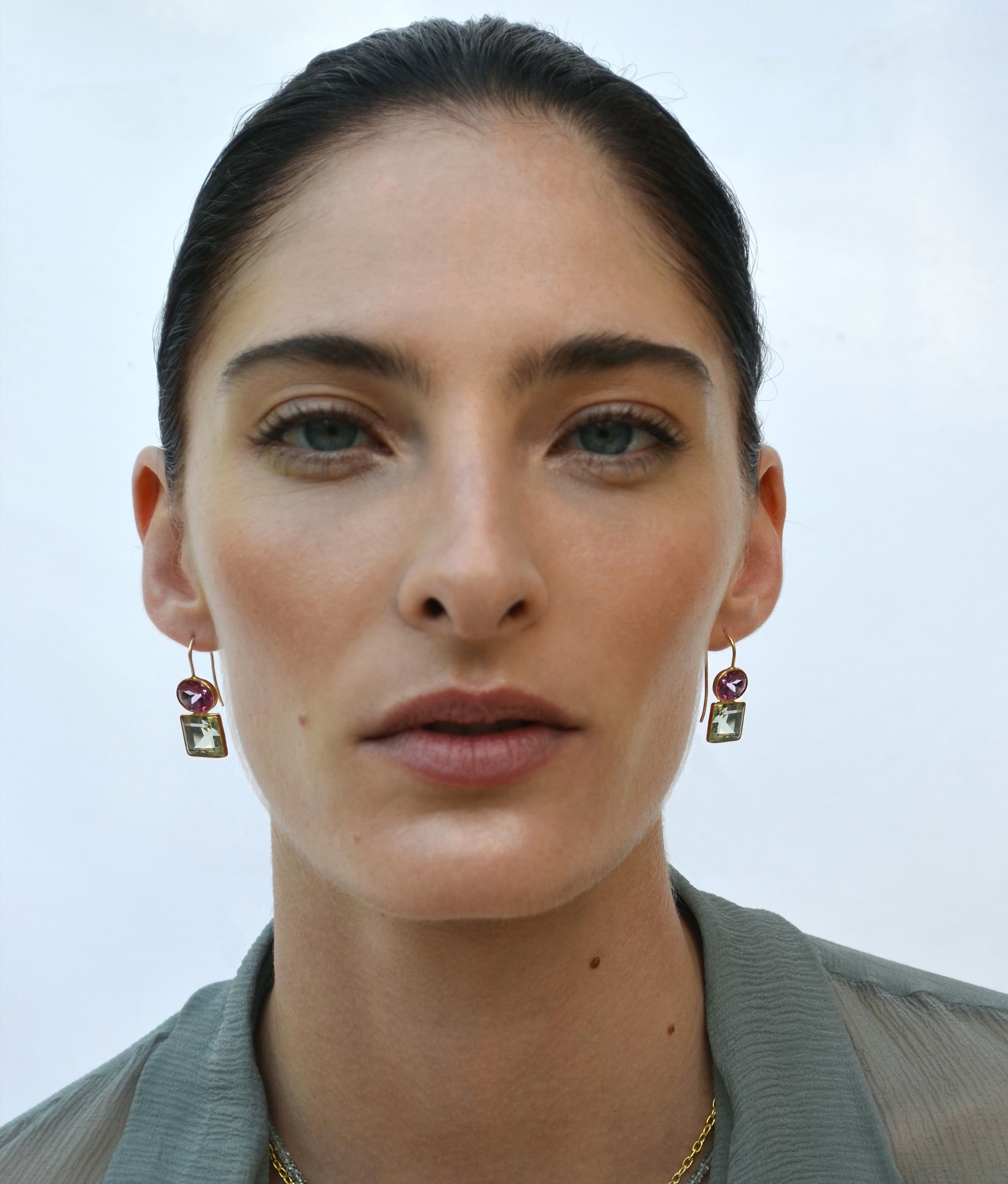 Model on blue backdrop wears gauzy top with Duo Earrings in Pink Topaz and Green Amethyst