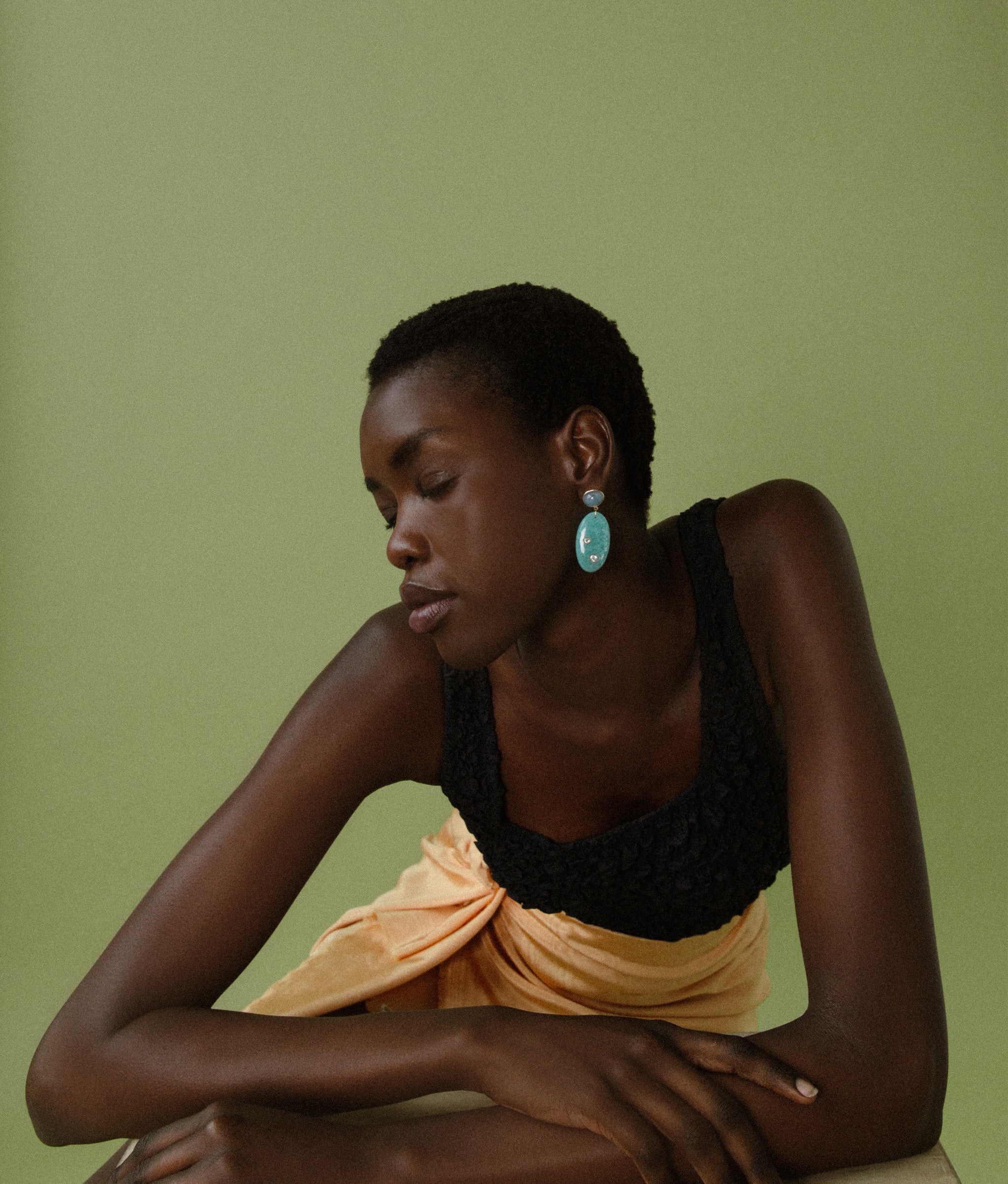 Model on green backdrop wears black tank, gold wrap skirt and 14k Gold, Aquamarine & Amazonite Earrings.