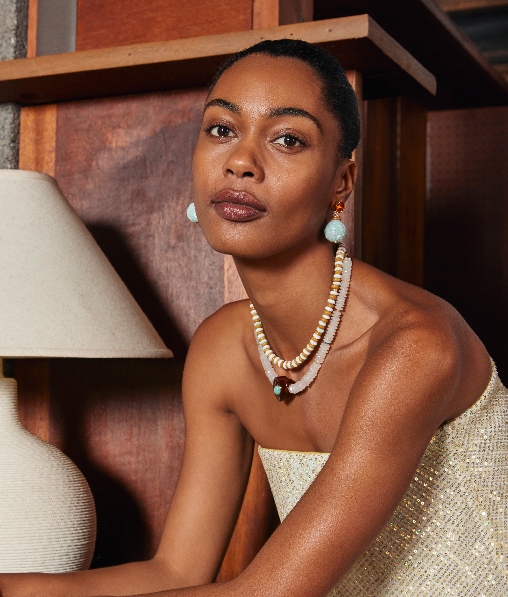 Model in living room wears sparkly strapless top with Gemini Collar, Moritz Necklace and Mist Drop Earrings.