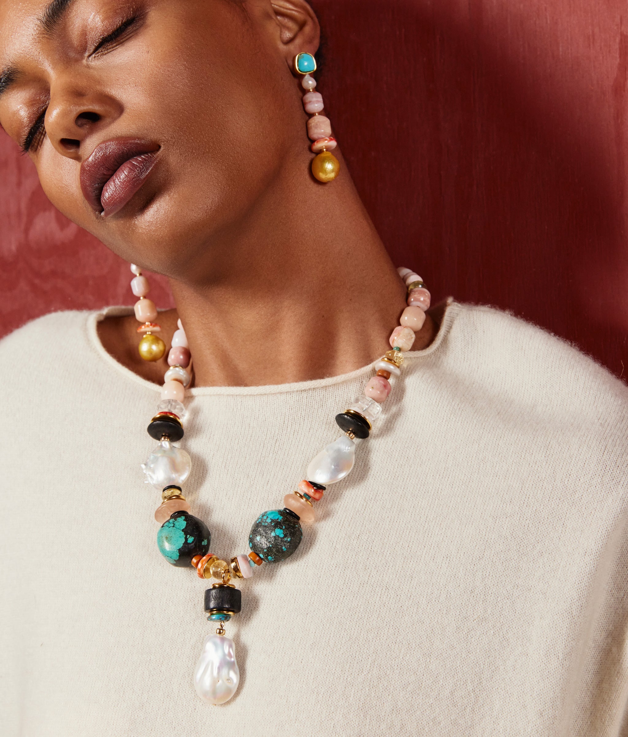 Model on burgundy backdrop wears cream knit with Forms in Nature Necklace and Navya Earrings.