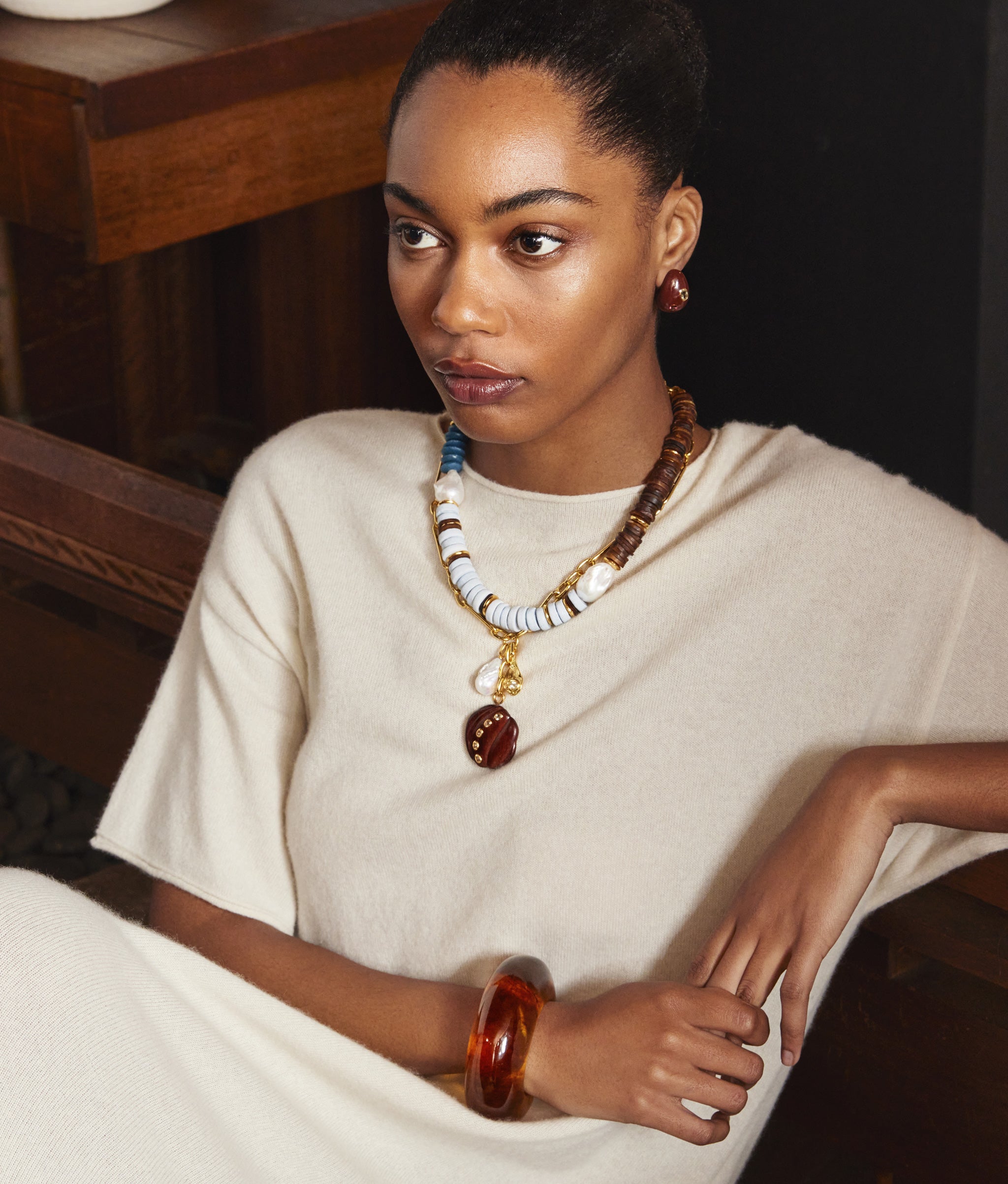 Model in cream knit dress wears Composition Necklace, Tavira Necklace in Coast, and Mini Arp Earrings in Studded Brown
