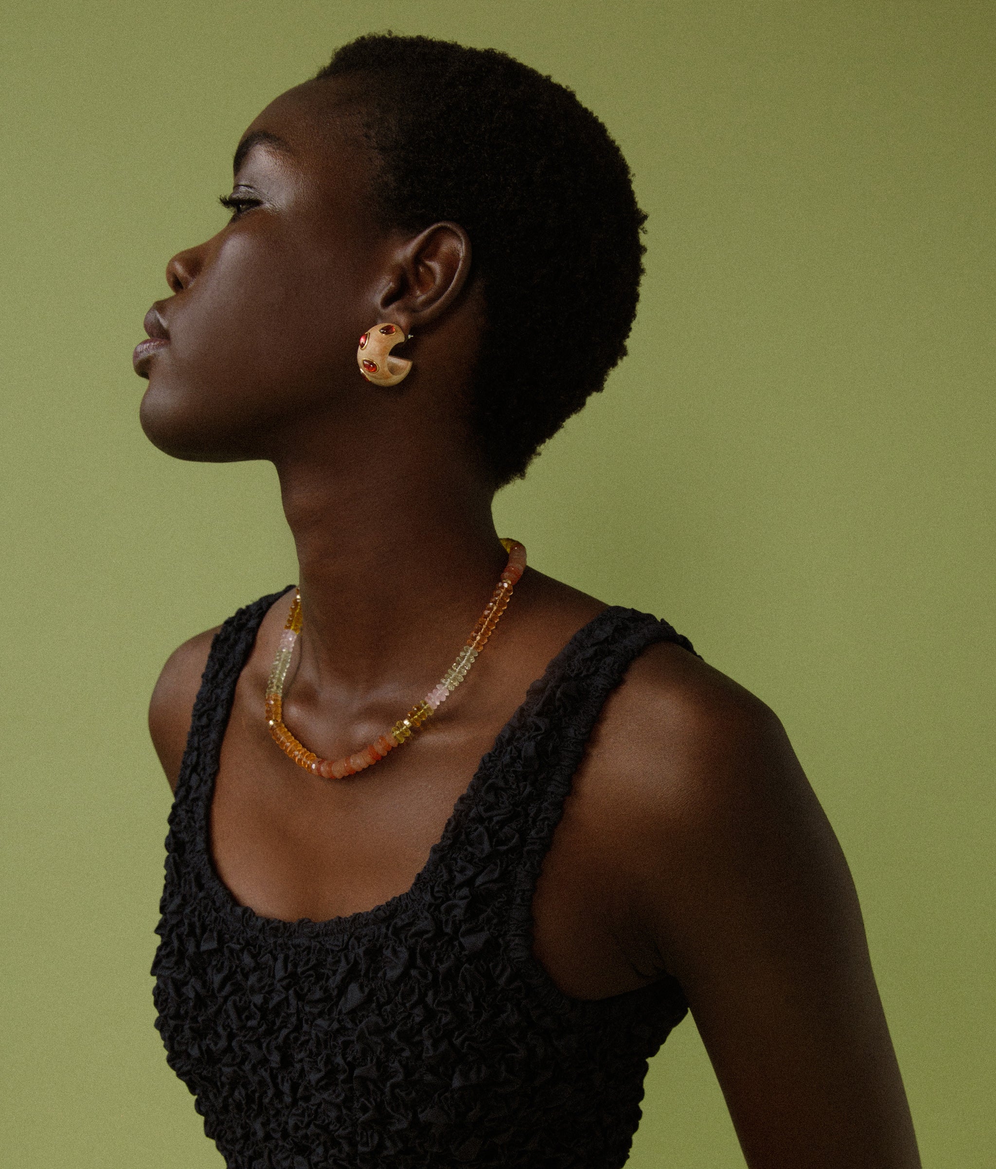 Model on green backdrop wears black bodysuit with Acacia Earrings in Pink Rhodolite and Selena Necklace in Sunrise.