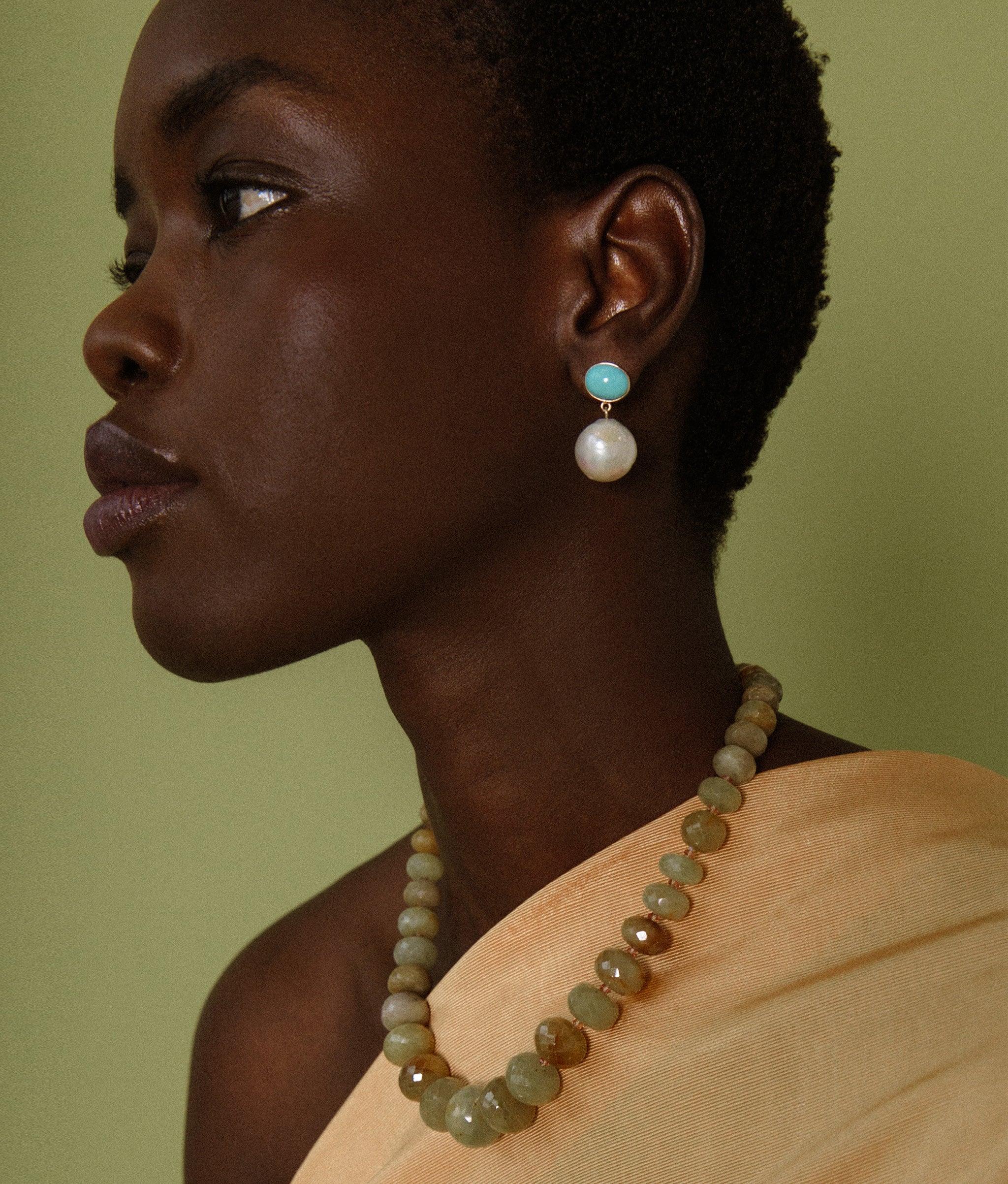 Model on green backdrop wears Large Graduated Yellow Sapphire & 14k Gold Necklace with turquoise and pearl earrings