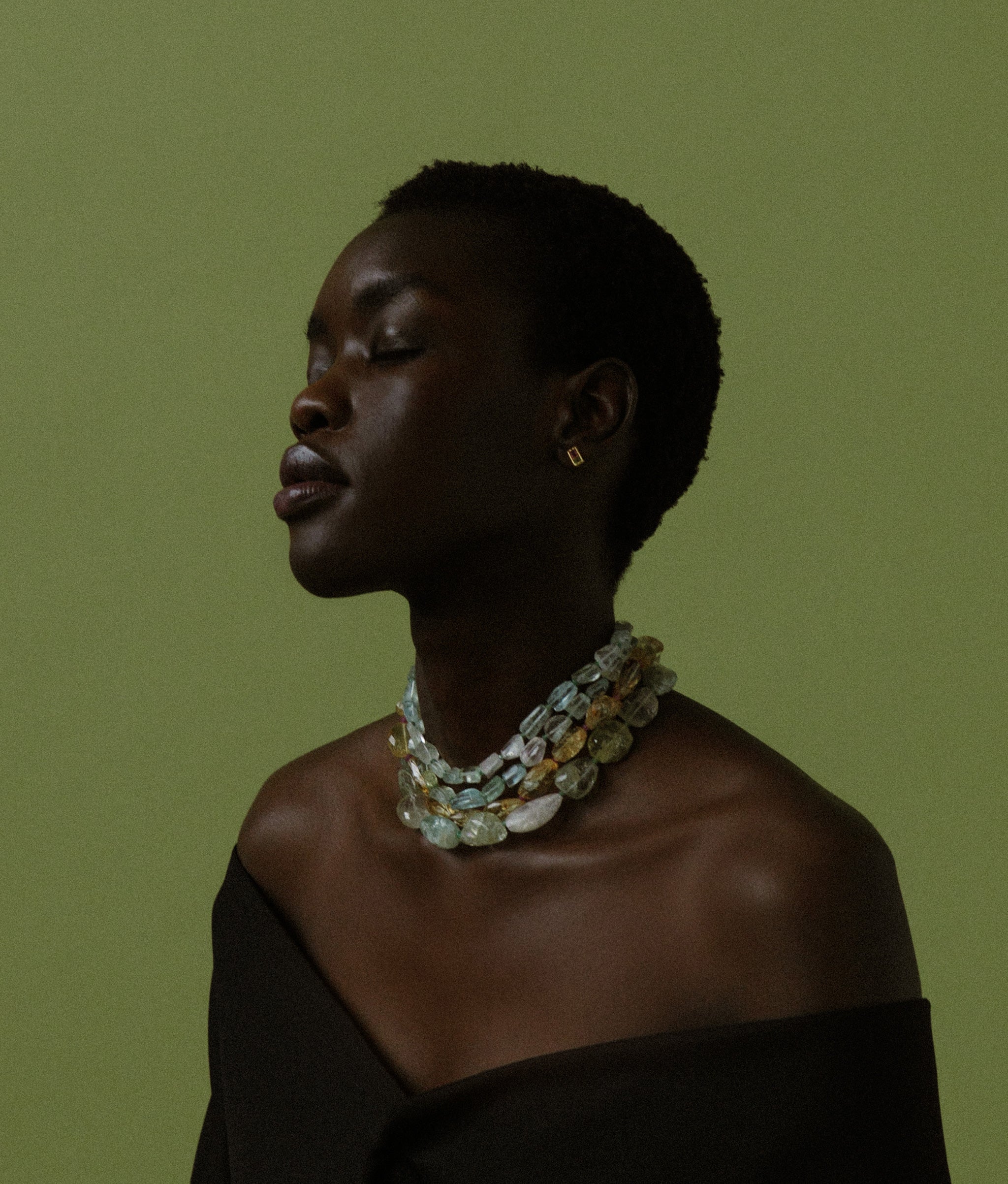 Model on green backdrop wears Small Faceted Aquamarine Nugget, Emerald & 14k Gold Necklace layered with other necklaces