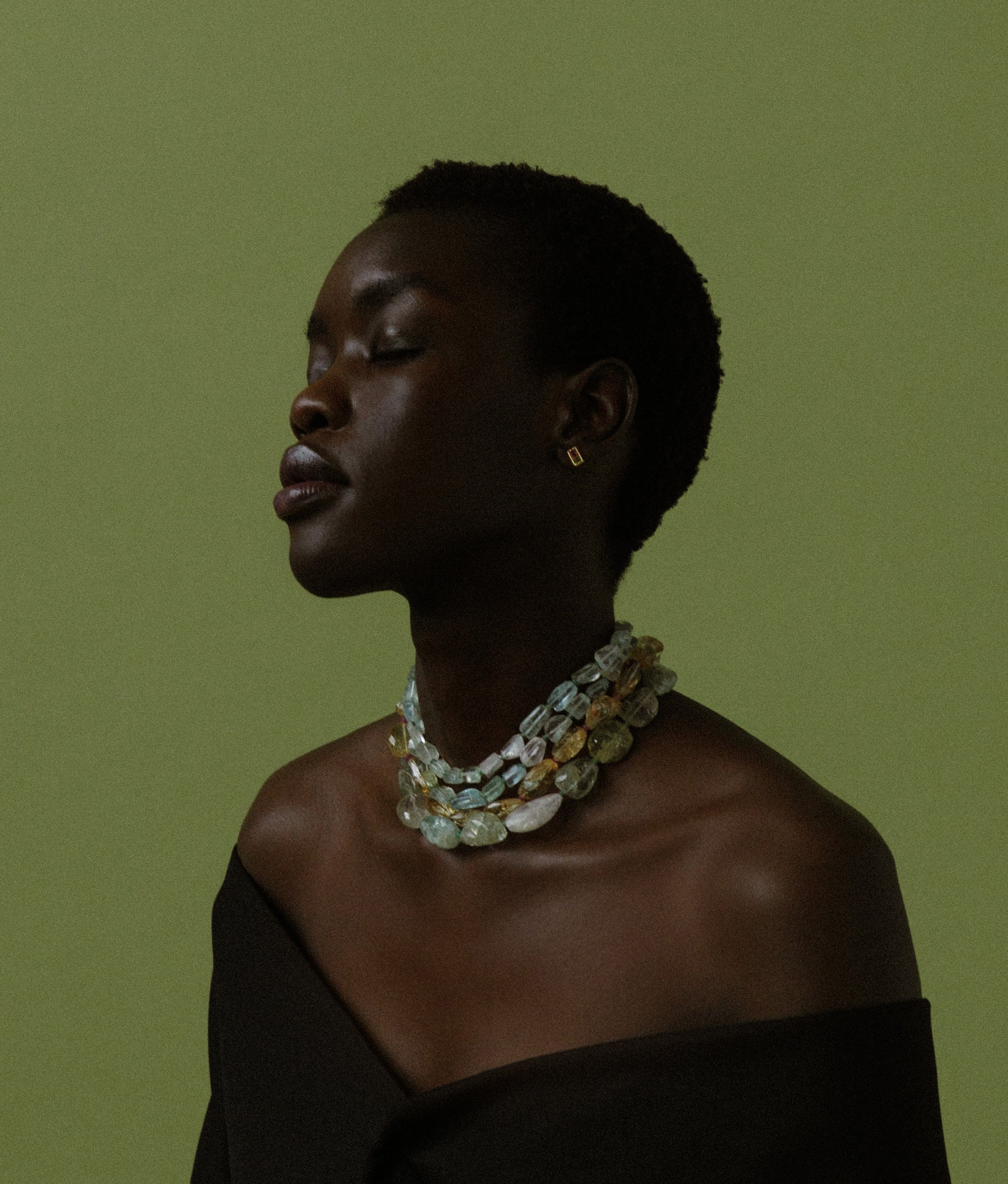Model on green backdrop wears Large Faceted Aquamarine Nugget, Emerald & 14k Gold Necklace layered with other necklaces