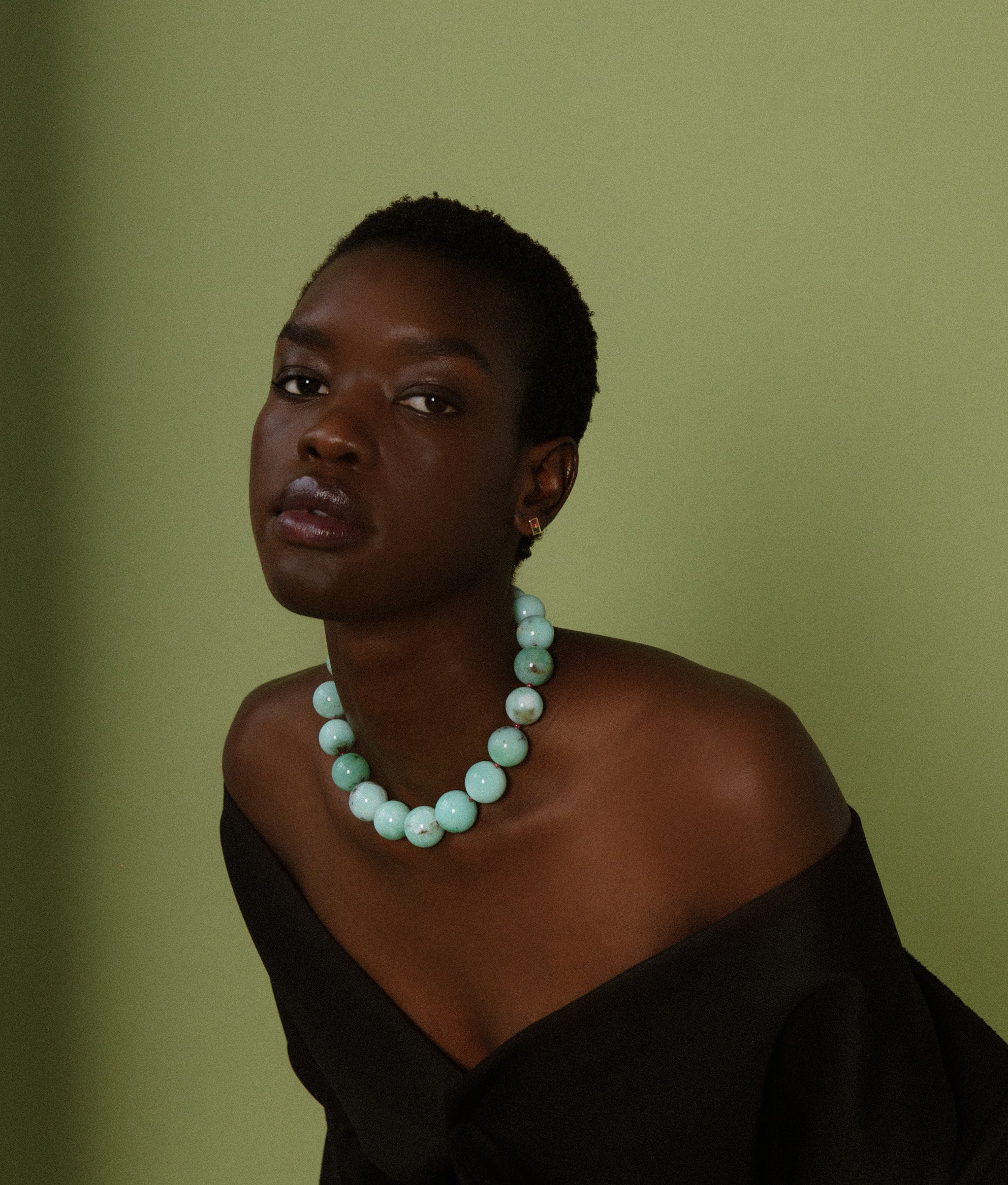 Model on green backdrop wears off-shoulder black top with Jumbo Chrysoprase, Ruby & 14k Gold Necklace.