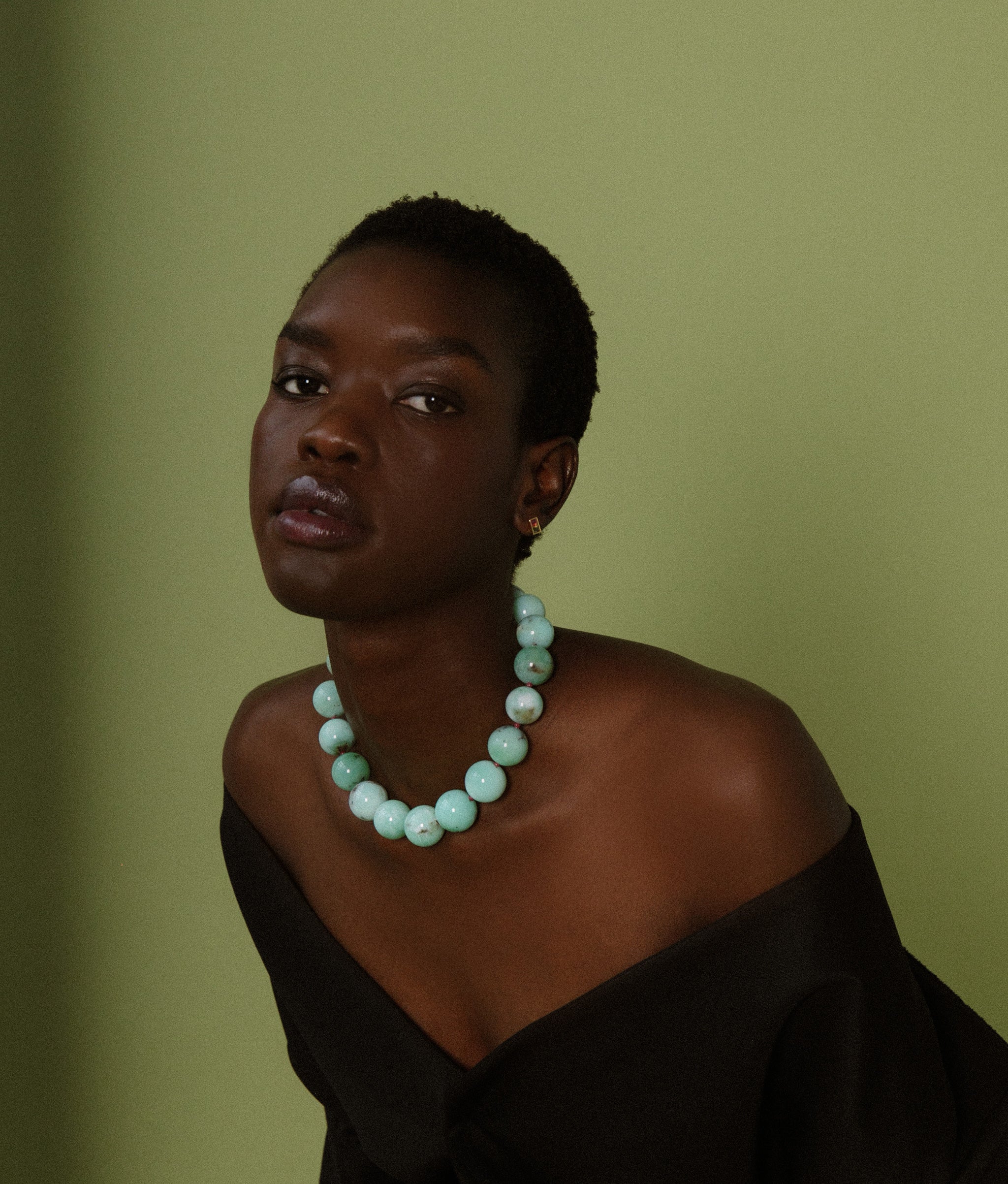 Model on green backdrop wears off-shoulder black top with Jumbo Chrysoprase, Ruby & 14k Gold Necklace. 