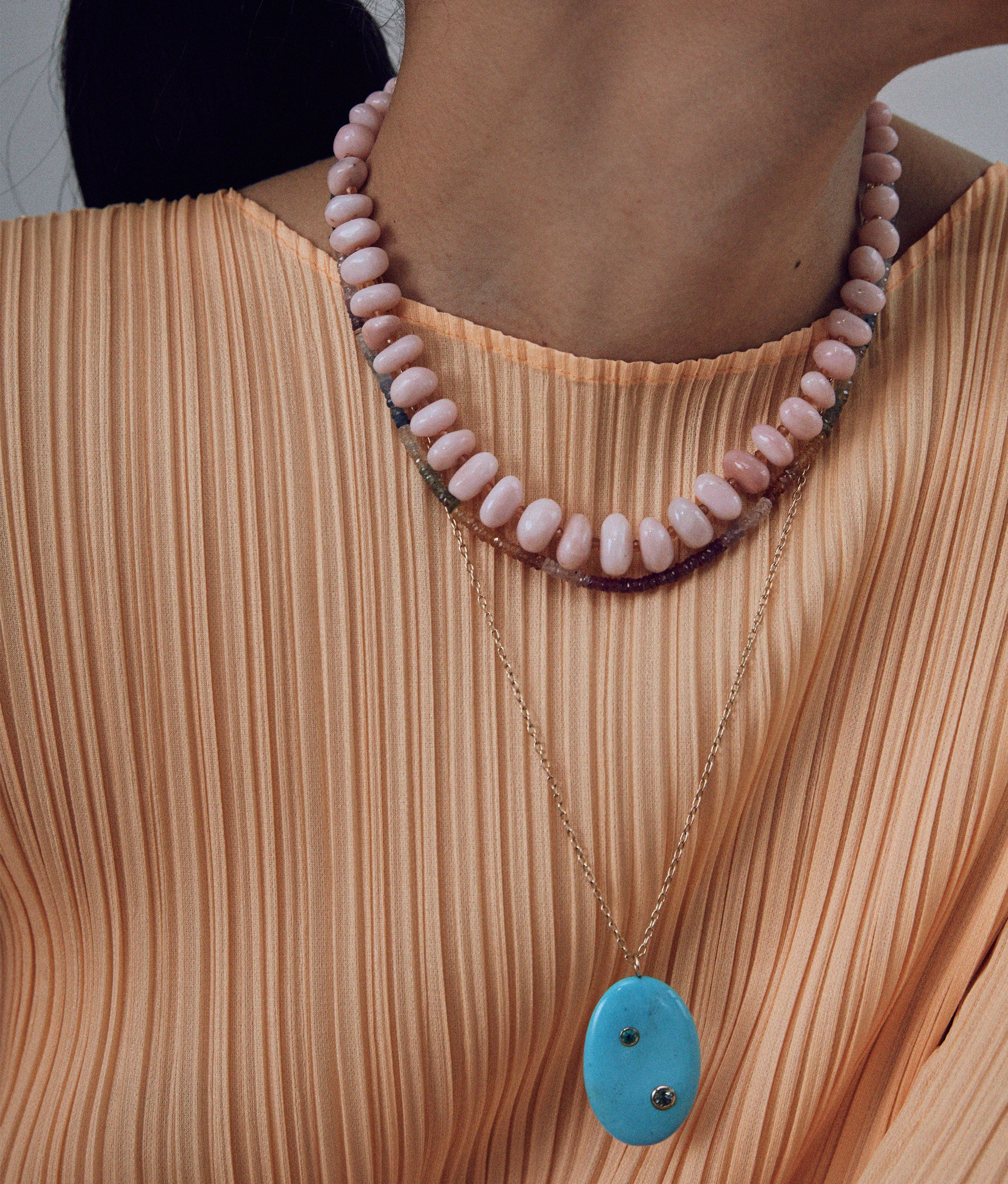 Close-up of Pink Opal & Yellow Sapphire 14k Gold Necklace contrasting pleated orange top.