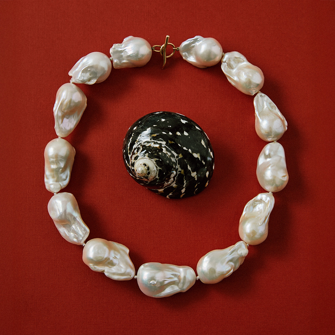 Flatlay on red background with black shell and Extra Large White Baroque Pearl Necklace