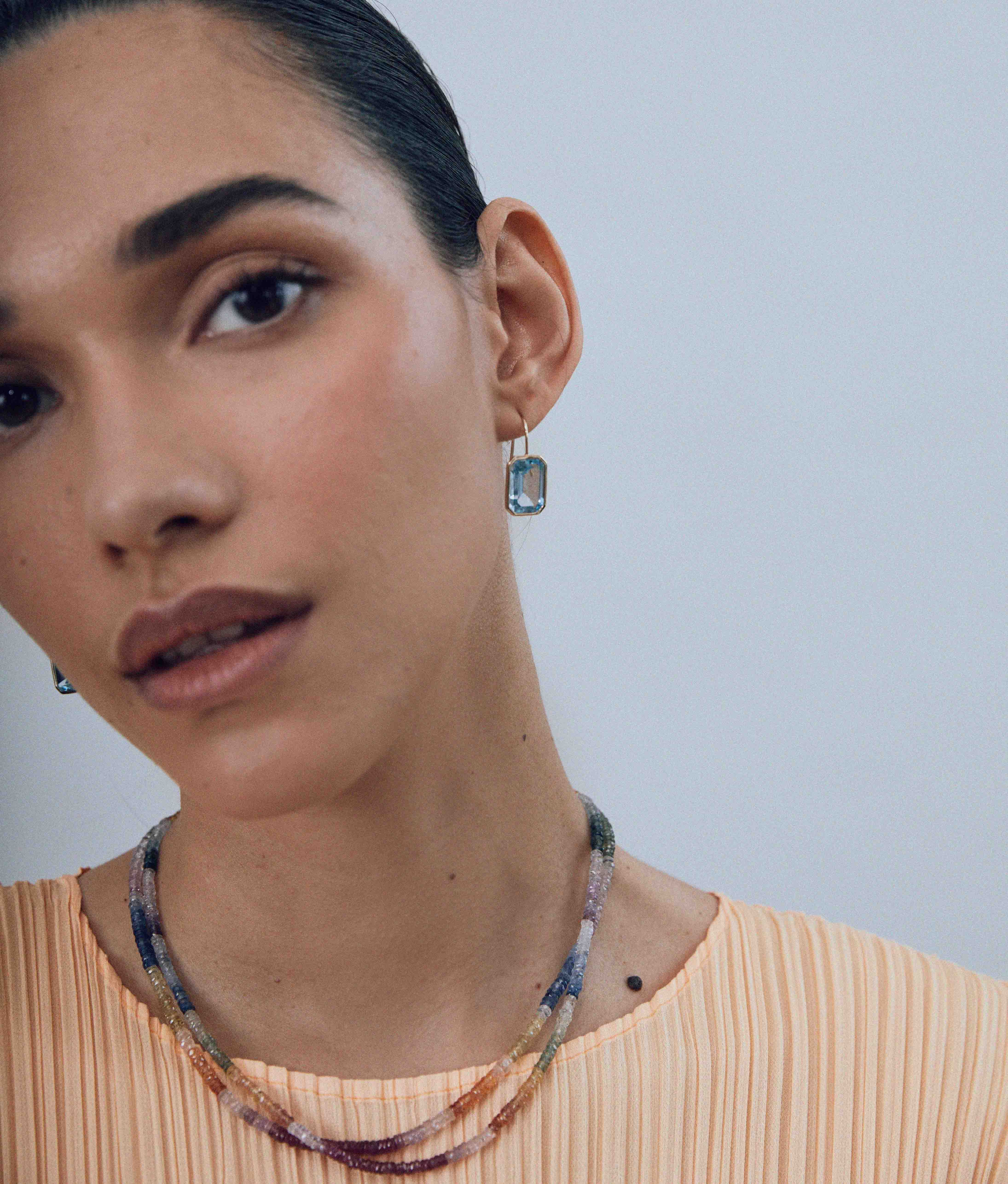 Model on grey background with the Brilliant Shaded Sapphire & 14k Gold Necklace and Aria Earrings in Sky Blue Topaz.